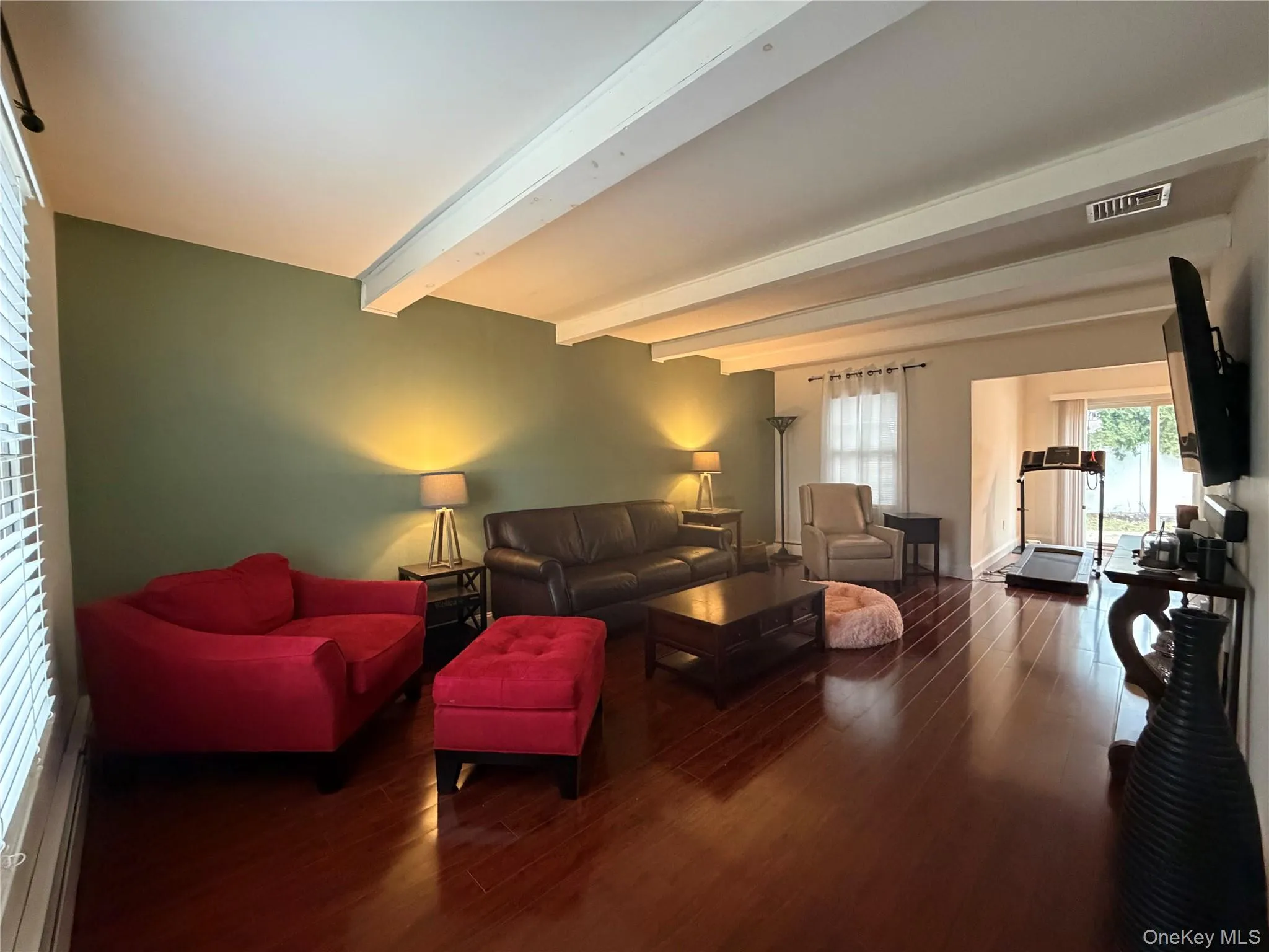 The living space features hardwood floors, exposed ceiling beams, and a window with blinds The living space features hardwood floors, exposed ceiling beams, and a window with blinds