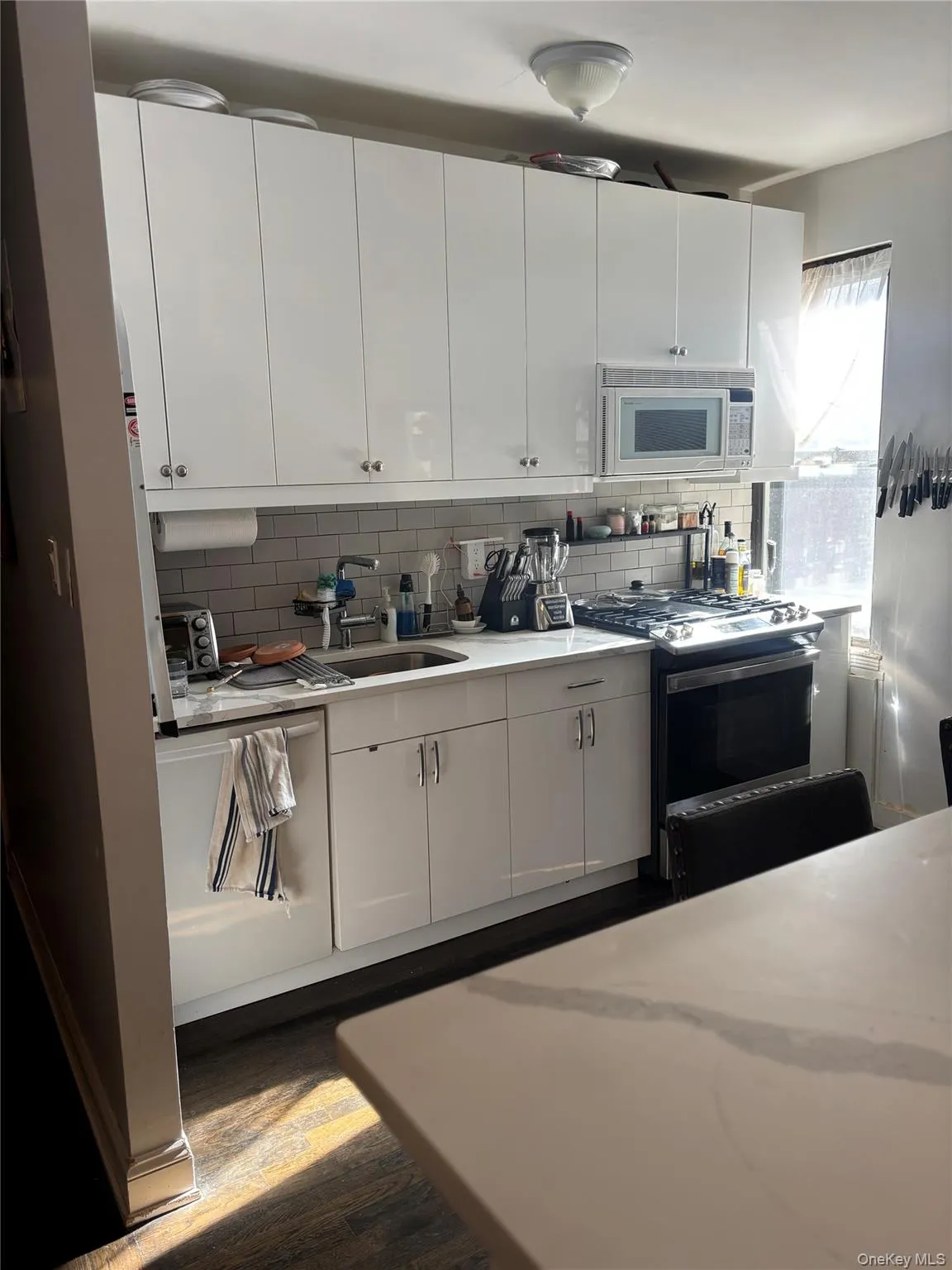 The kitchen features white cabinetry, a white subway tile backsplash, a stainless steel microwave, and a dark-colored range The kitchen features white cabinetry, a white subway tile backsplash, a stainless steel microwave, and a dark-colored range