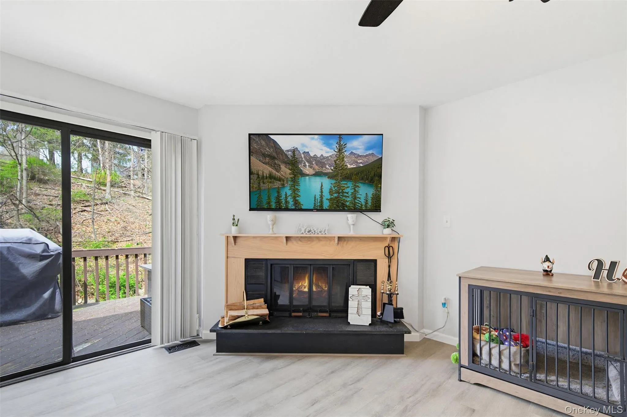 Living area with light-toned flooring, a wood burning fireplace with a light wood mantel, and sliding glass doors that open to a deck Living area with light-toned flooring, a wood burning fireplace with a light wood mantel, and sliding glass doors that open to a deck
