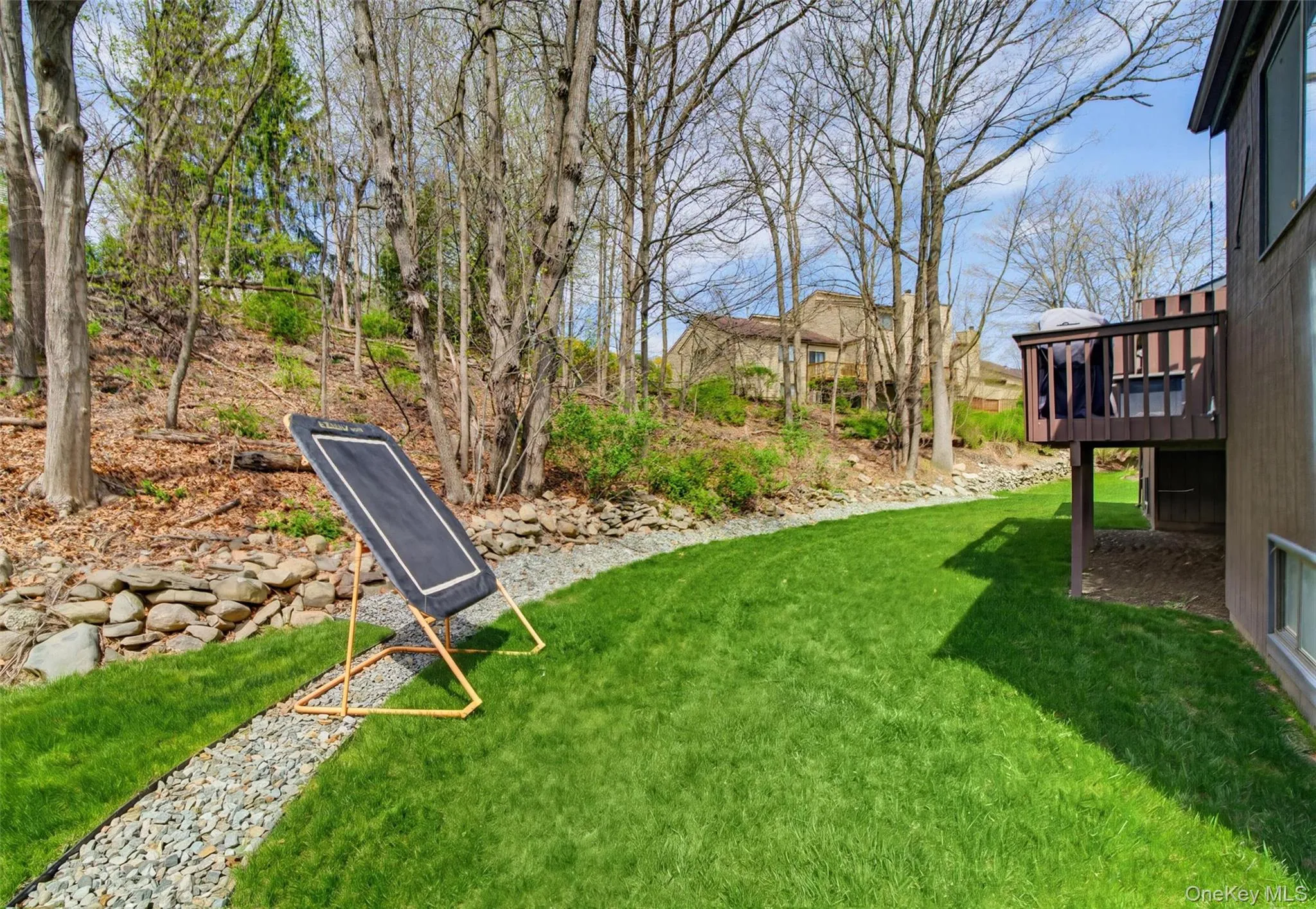 The property features a well-maintained lawn, a stone retaining wall, and mature trees, with a deck providing outdoor living space The property features a well-maintained lawn, a stone retaining wall, and mature trees, with a deck providing outdoor living space