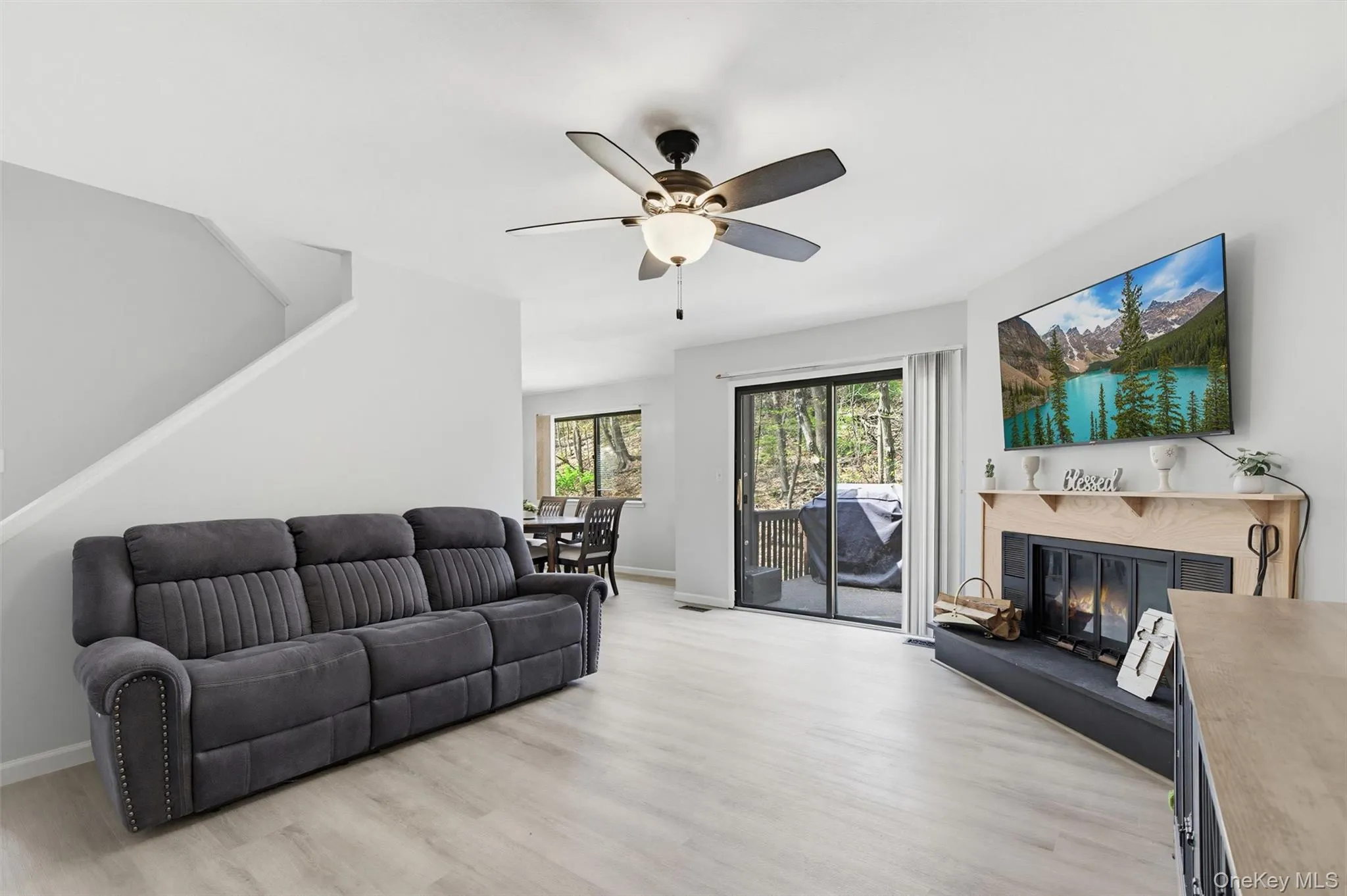 The inviting living area features light-colored flooring, a ceiling fan, and a fireplace with a mantel The inviting living area features light-colored flooring, a ceiling fan, and a fireplace with a mantel