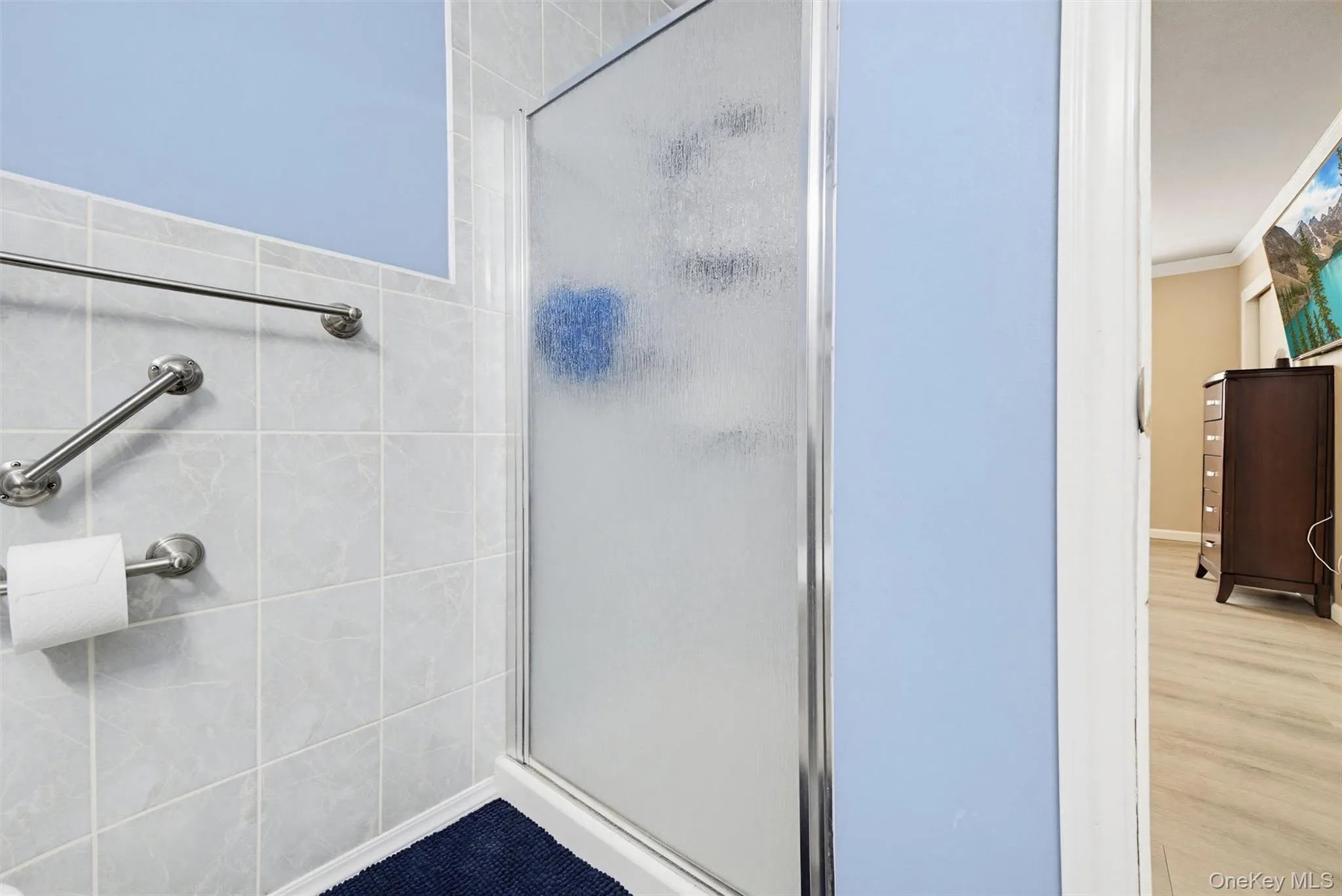 Bathroom featuring a shower with a frosted glass door, light blue wall paint, and light-colored square tiles Bathroom featuring a shower with a frosted glass door, light blue wall paint, and light-colored square tiles