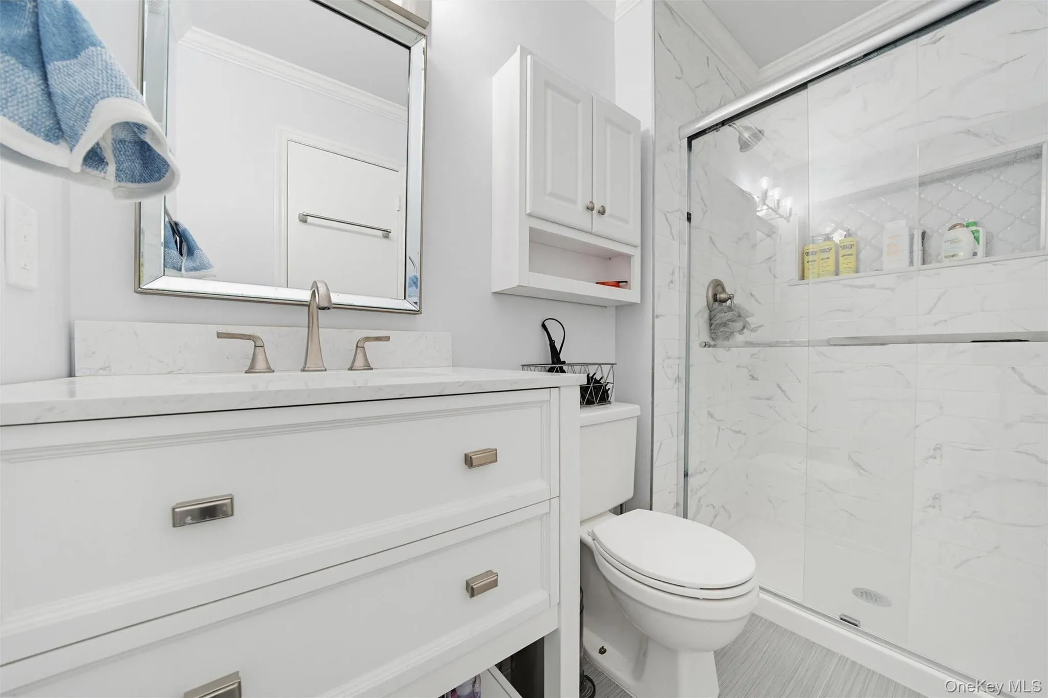 The bathroom features a white vanity with a marble-patterned countertop, a framed mirror, and a shower with sliding glass doors and marble-patterned tile The bathroom features a white vanity with a marble-patterned countertop, a framed mirror, and a shower with sliding glass doors and marble-patterned tile