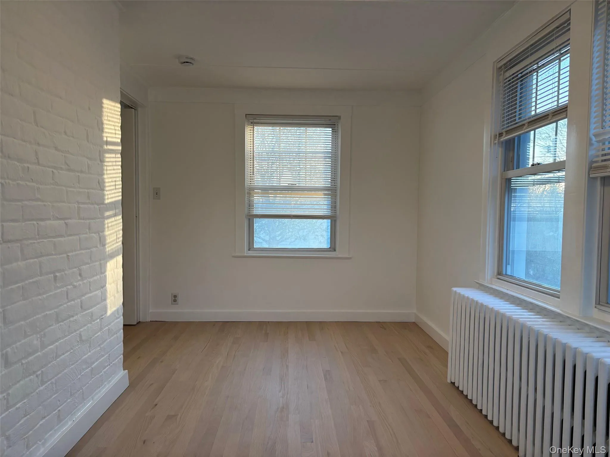 This room features hardwood floors, white painted walls, and a white painted brick wall This room features hardwood floors, white painted walls, and a white painted brick wall