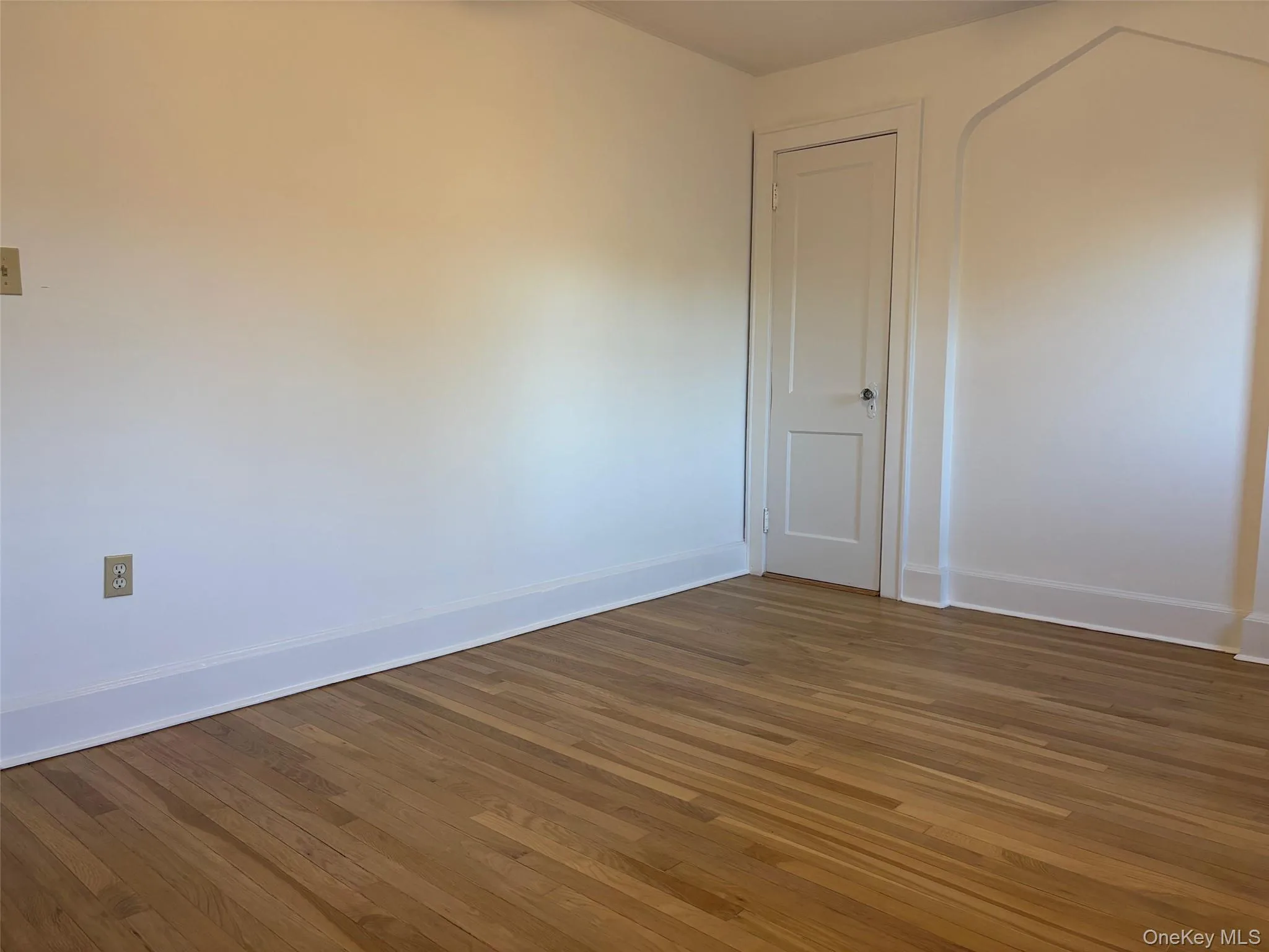The room features hardwood floors, white baseboards, and a white interior door The room features hardwood floors, white baseboards, and a white interior door