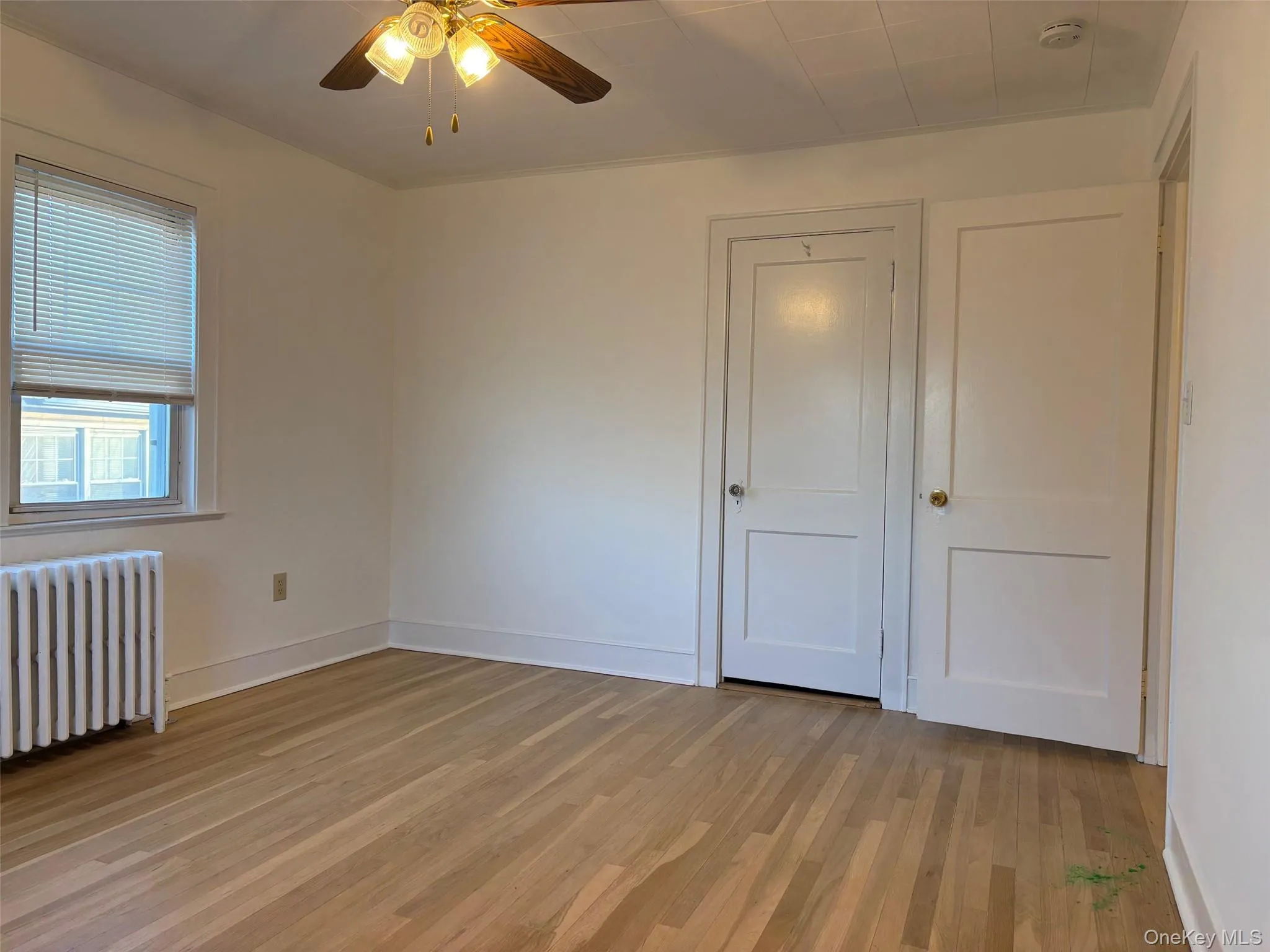 This room features hardwood flooring, a window with blinds, and white doors with brass-toned knobs This room features hardwood flooring, a window with blinds, and white doors with brass-toned knobs