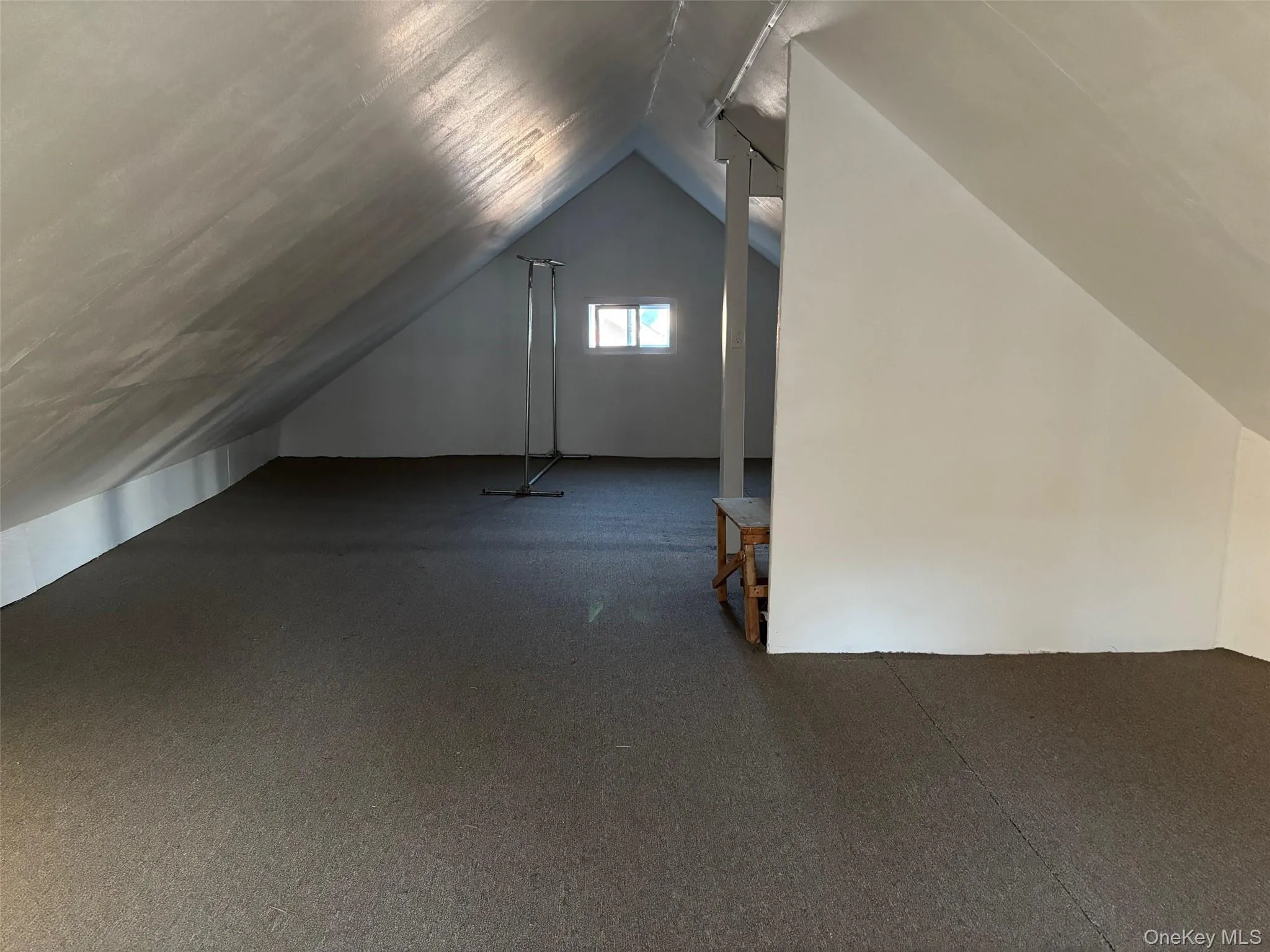 The property features an expansive attic space with sloped ceilings, a window, and a dark carpeted floor The property features an expansive attic space with sloped ceilings, a window, and a dark carpeted floor