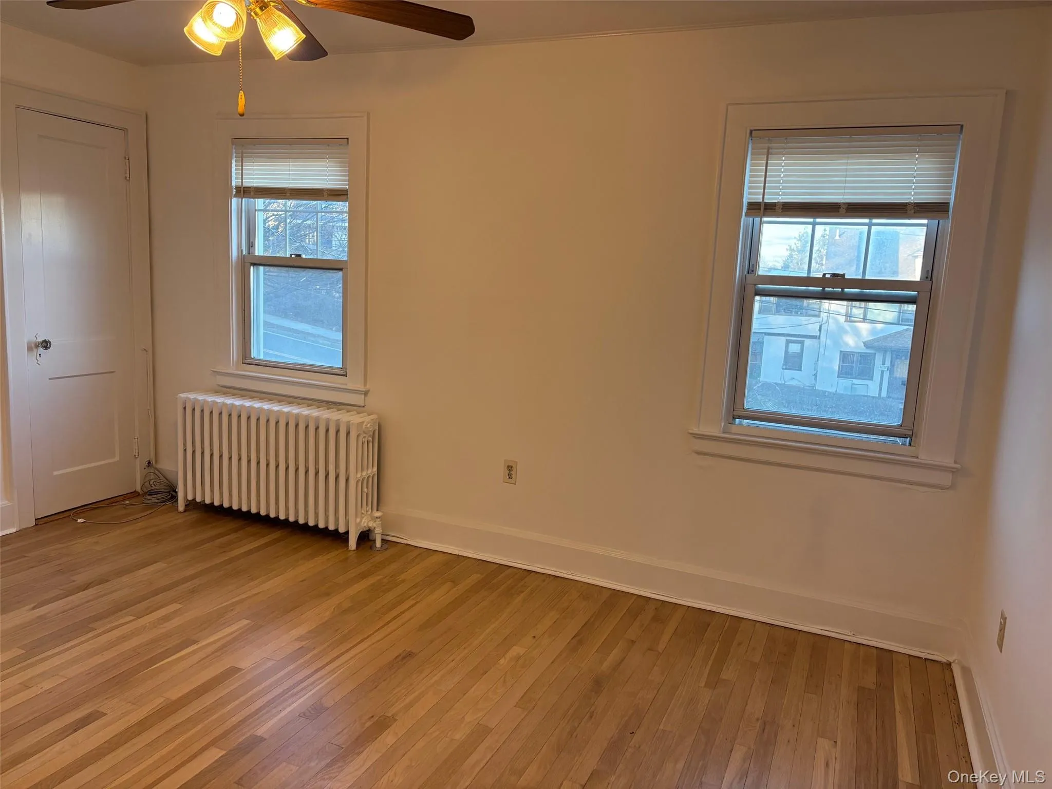 The room features hardwood floors, light-colored walls, and two windows providing natural light The room features hardwood floors, light-colored walls, and two windows providing natural light