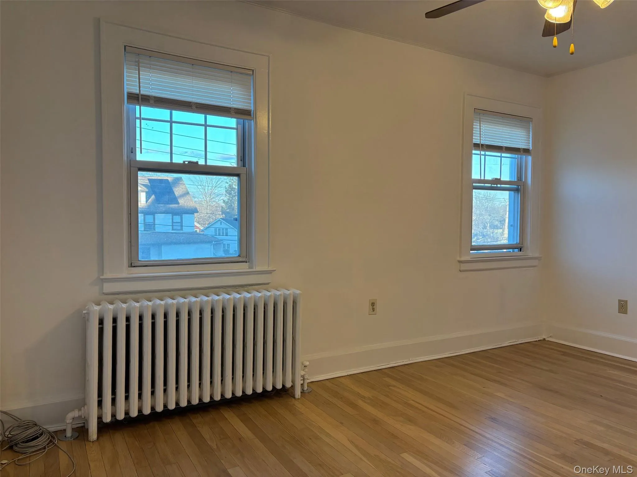 This room features two windows, hardwood floors, and a ceiling fan with a light fixture This room features two windows, hardwood floors, and a ceiling fan with a light fixture