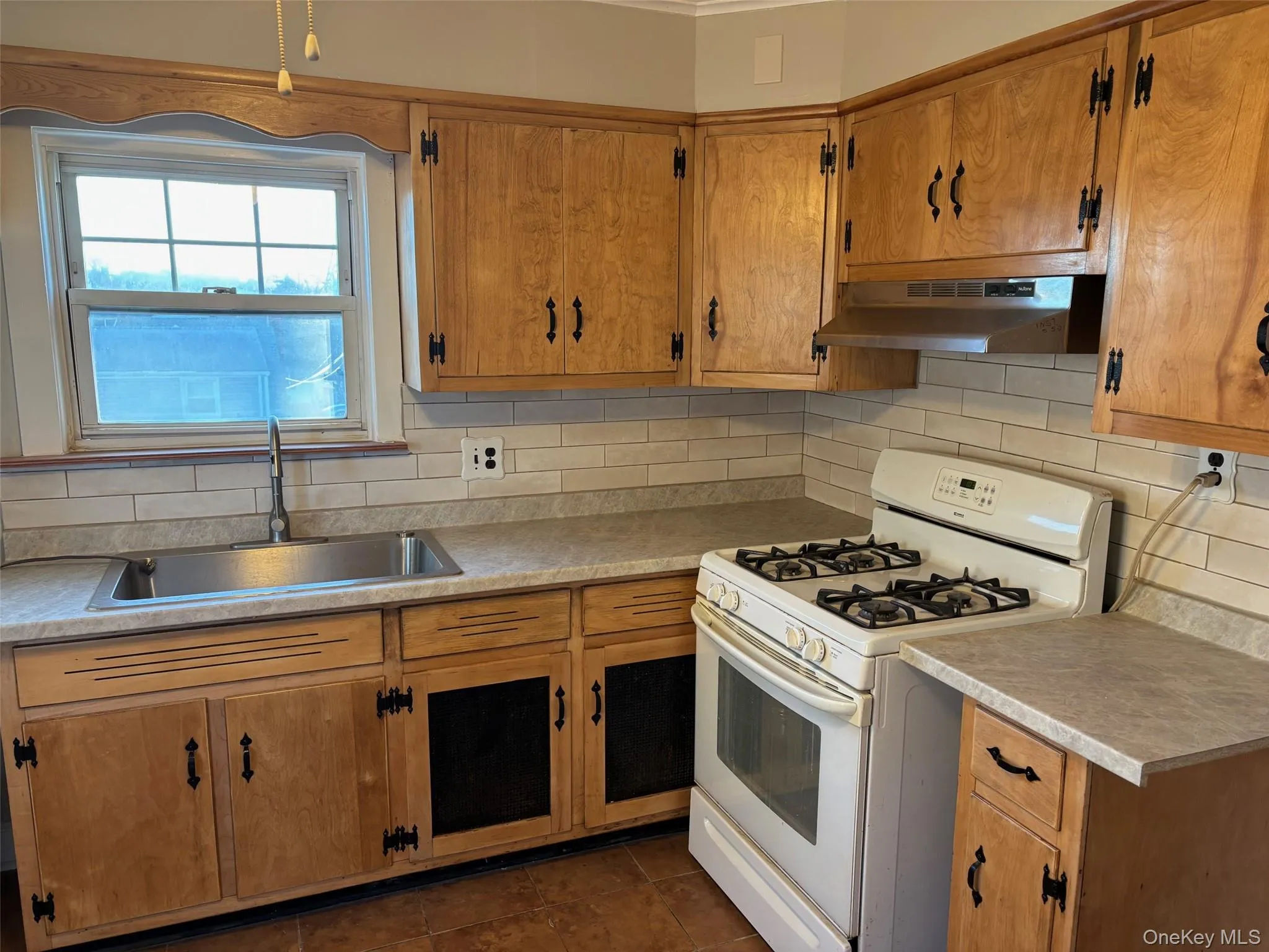 Kitchen featuring wood cabinetry, a stainless steel sink, a subway tile backsplash, and a white gas range with an overhead range hood Kitchen featuring wood cabinetry, a stainless steel sink, a subway tile backsplash, and a white gas range with an overhead range hood