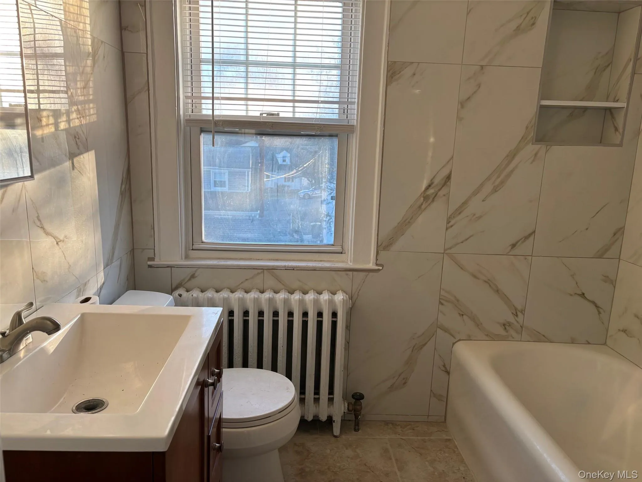 The bathroom features a vanity with a rectangular sink, a toilet, a bathtub, and tiled walls with a built-in shelf The bathroom features a vanity with a rectangular sink, a toilet, a bathtub, and tiled walls with a built-in shelf