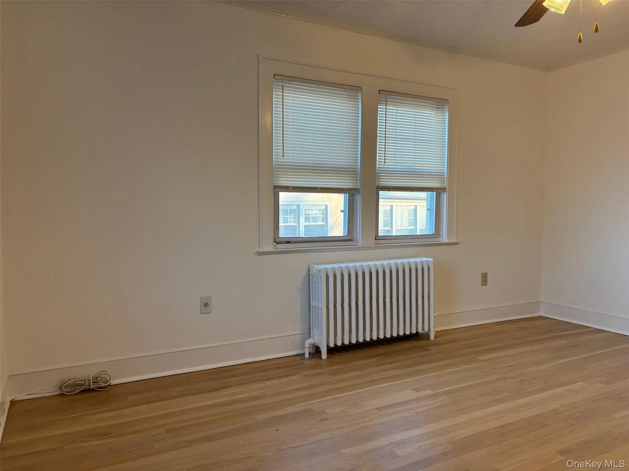 This room features light-toned hardwood flooring, a window with horizontal blinds, and a classic white radiator below the window This room features light-toned hardwood flooring, a window with horizontal blinds, and a classic white radiator below the window