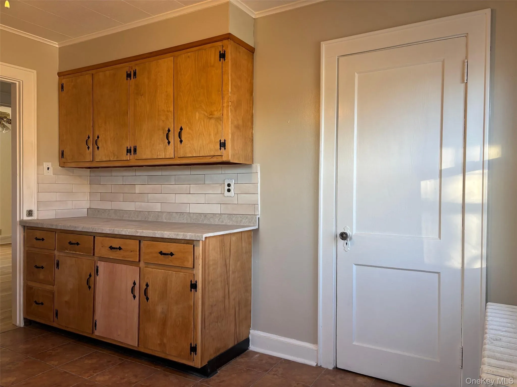 The kitchen features wood cabinetry, a light-colored countertop, and a white subway tile backsplash The kitchen features wood cabinetry, a light-colored countertop, and a white subway tile backsplash