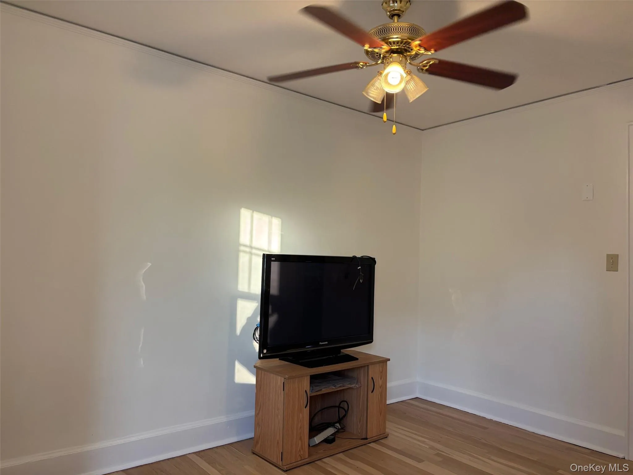 Room featuring light-colored walls, hardwood flooring, and a ceiling fan with light fixture Room featuring light-colored walls, hardwood flooring, and a ceiling fan with light fixture