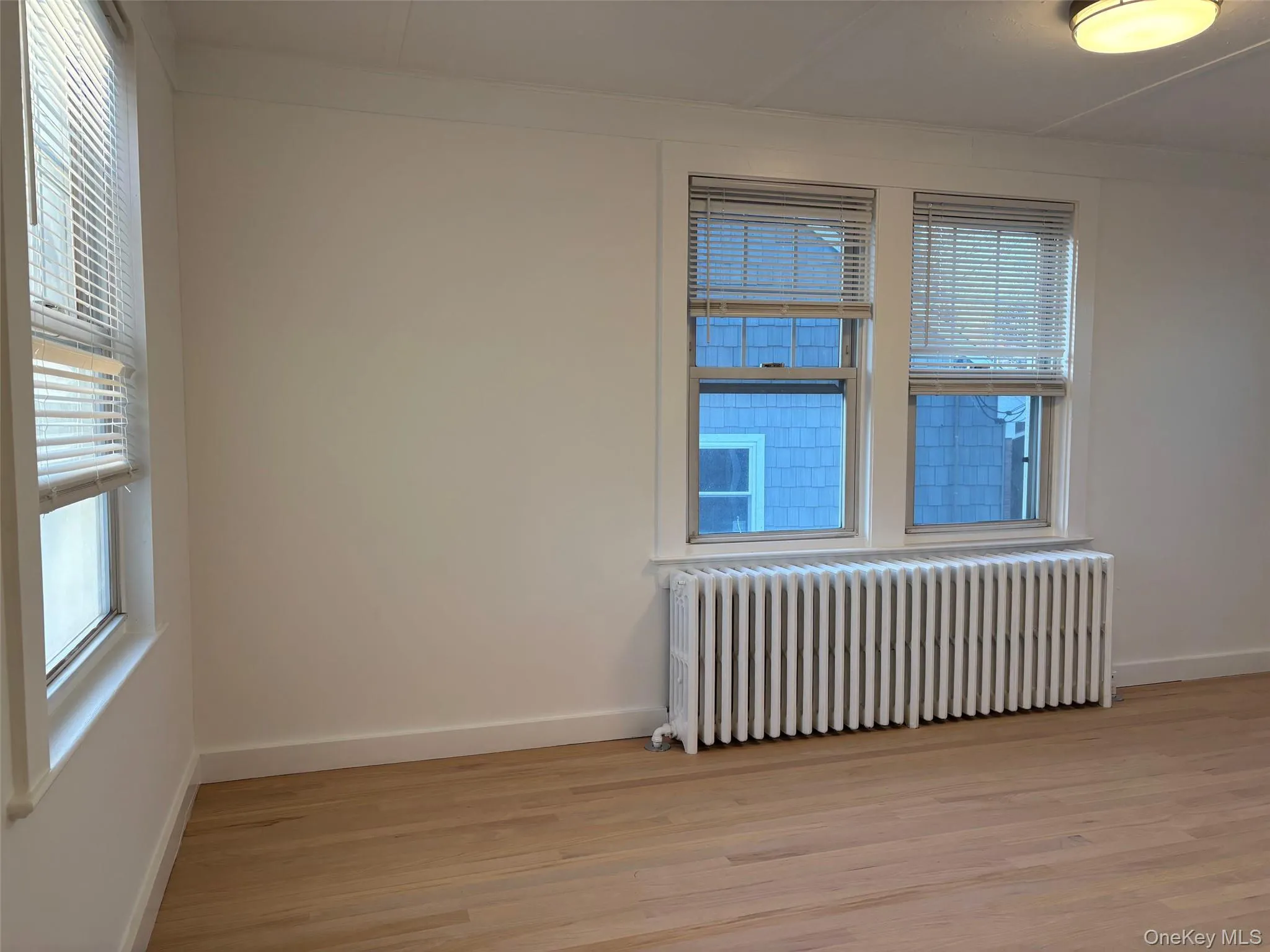 Room featuring light-colored hardwood floors, white walls, and bright windows with blinds Room featuring light-colored hardwood floors, white walls, and bright windows with blinds