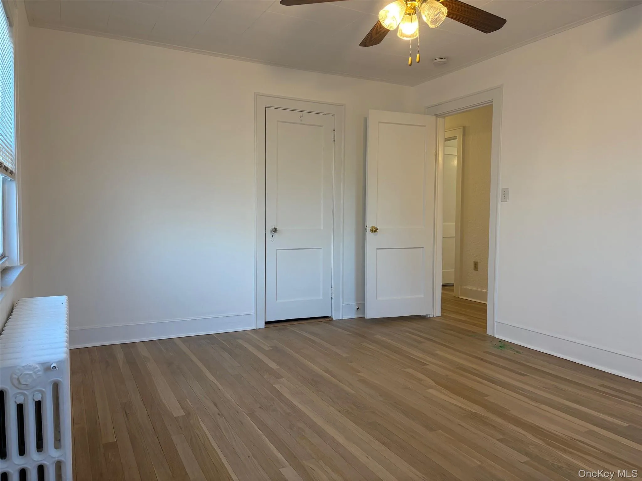 This room features hardwood floors, a ceiling fan with integrated lighting, and white walls This room features hardwood floors, a ceiling fan with integrated lighting, and white walls