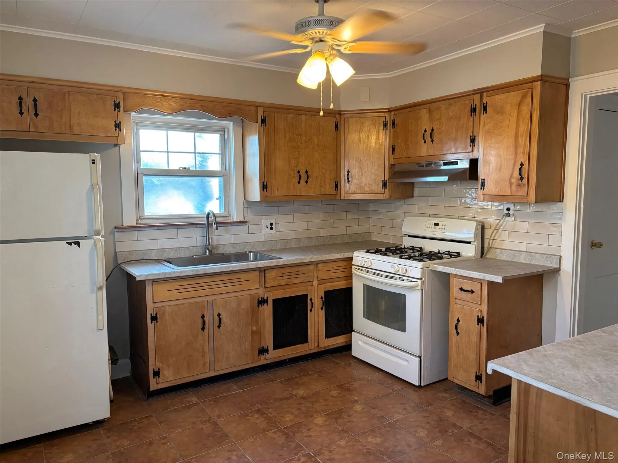 The kitchen features wood cabinetry, a tiled backsplash, and a ceiling fan with light fixtures The kitchen features wood cabinetry, a tiled backsplash, and a ceiling fan with light fixtures
