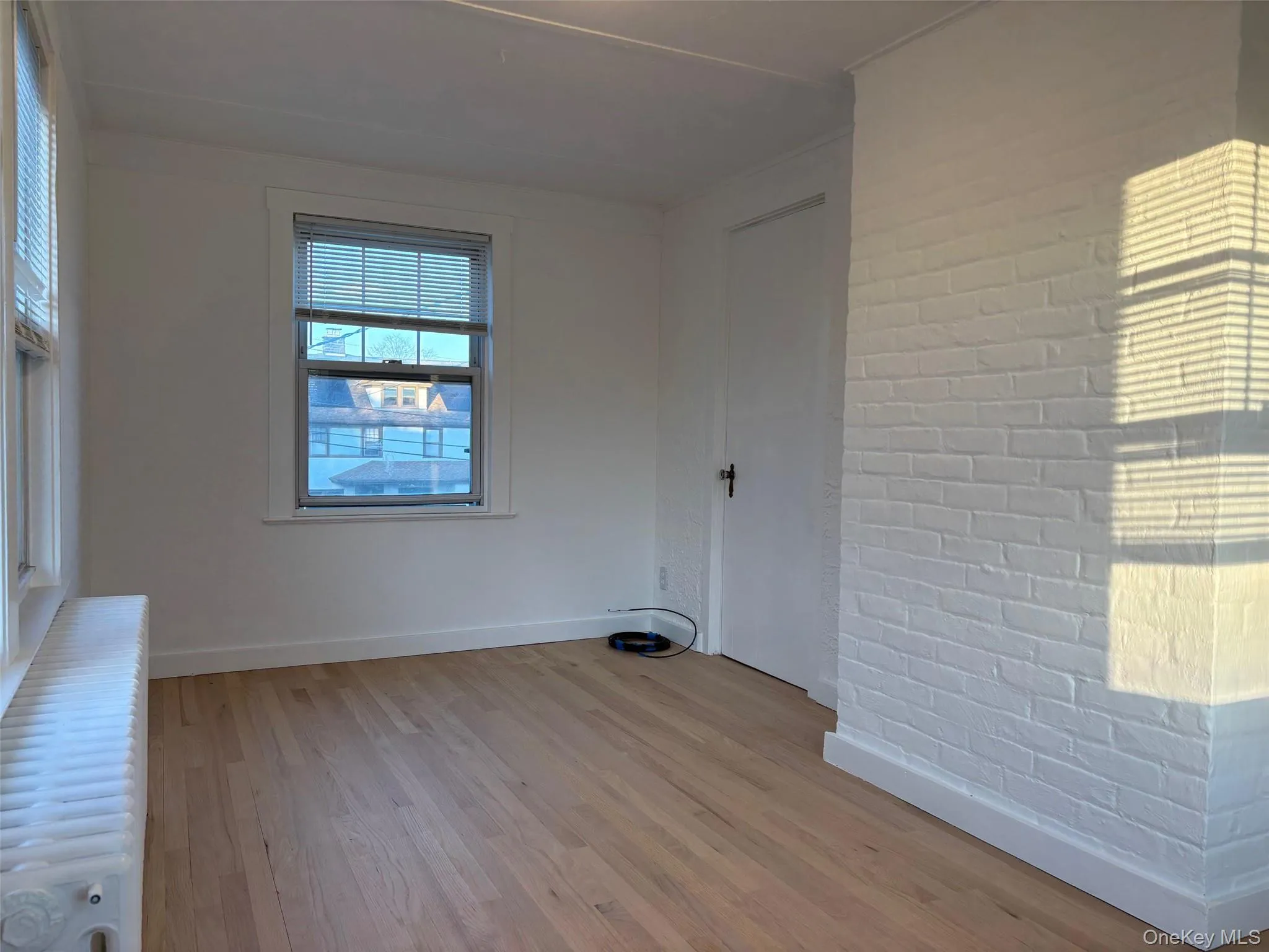 This room features light hardwood floors, white walls, and a white brick accent wall This room features light hardwood floors, white walls, and a white brick accent wall