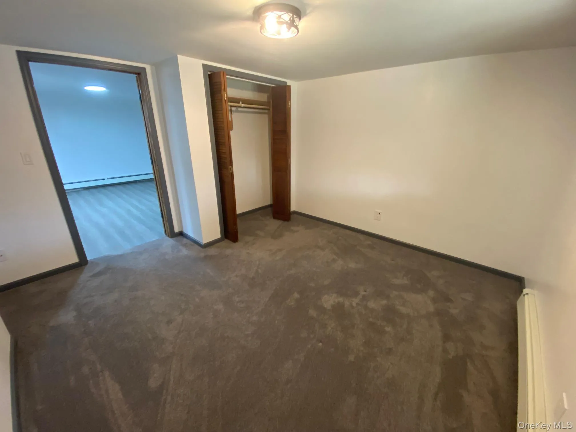 Unfurnished bedroom with dark colored carpet, a baseboard radiator, and a closet Unfurnished bedroom with dark colored carpet, a baseboard radiator, and a closet