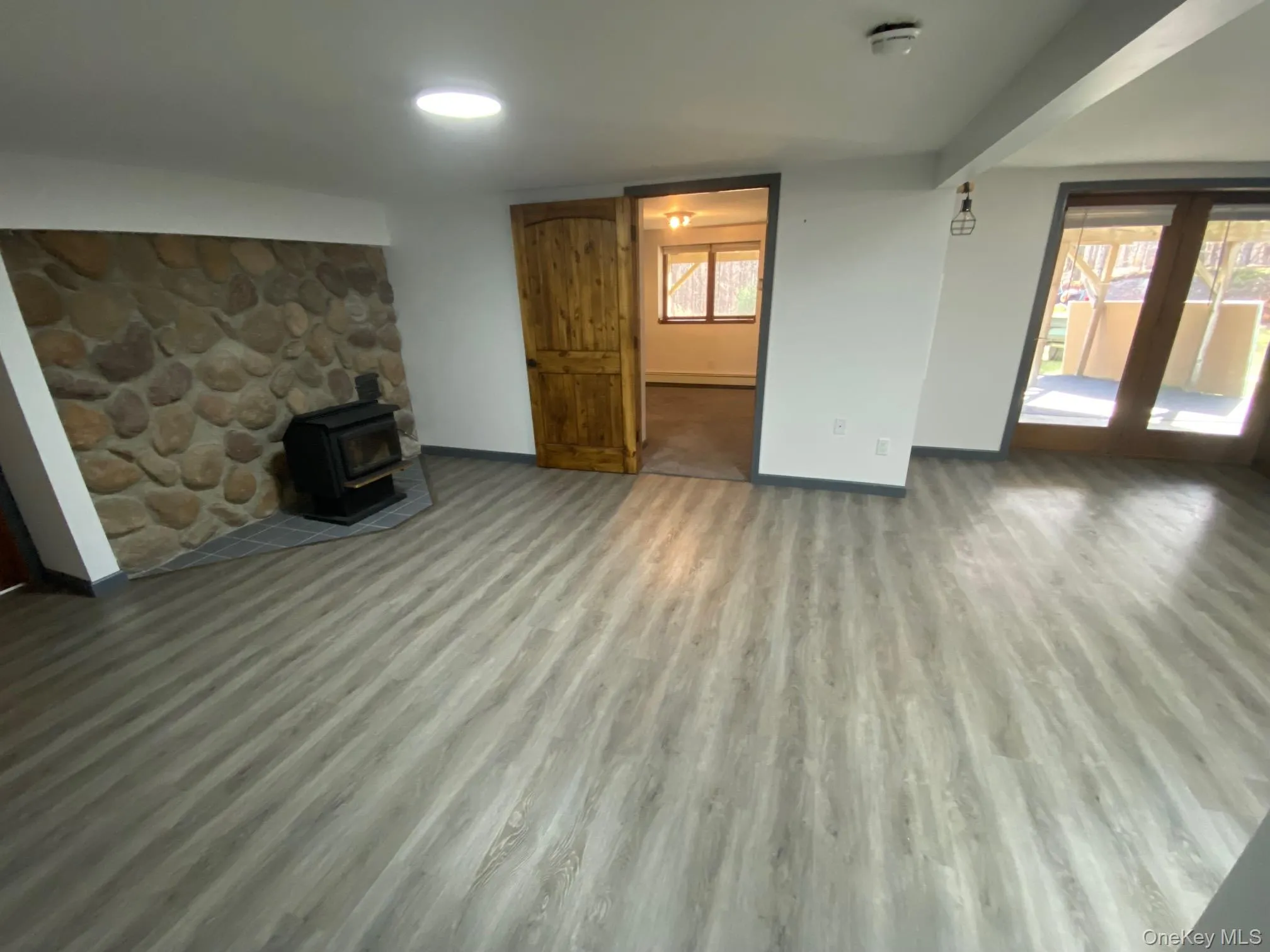Unfurnished living room featuring light wood-type flooring, a wood stove, and a wealth of natural light Unfurnished living room featuring light wood-type flooring, a wood stove, and a wealth of natural light