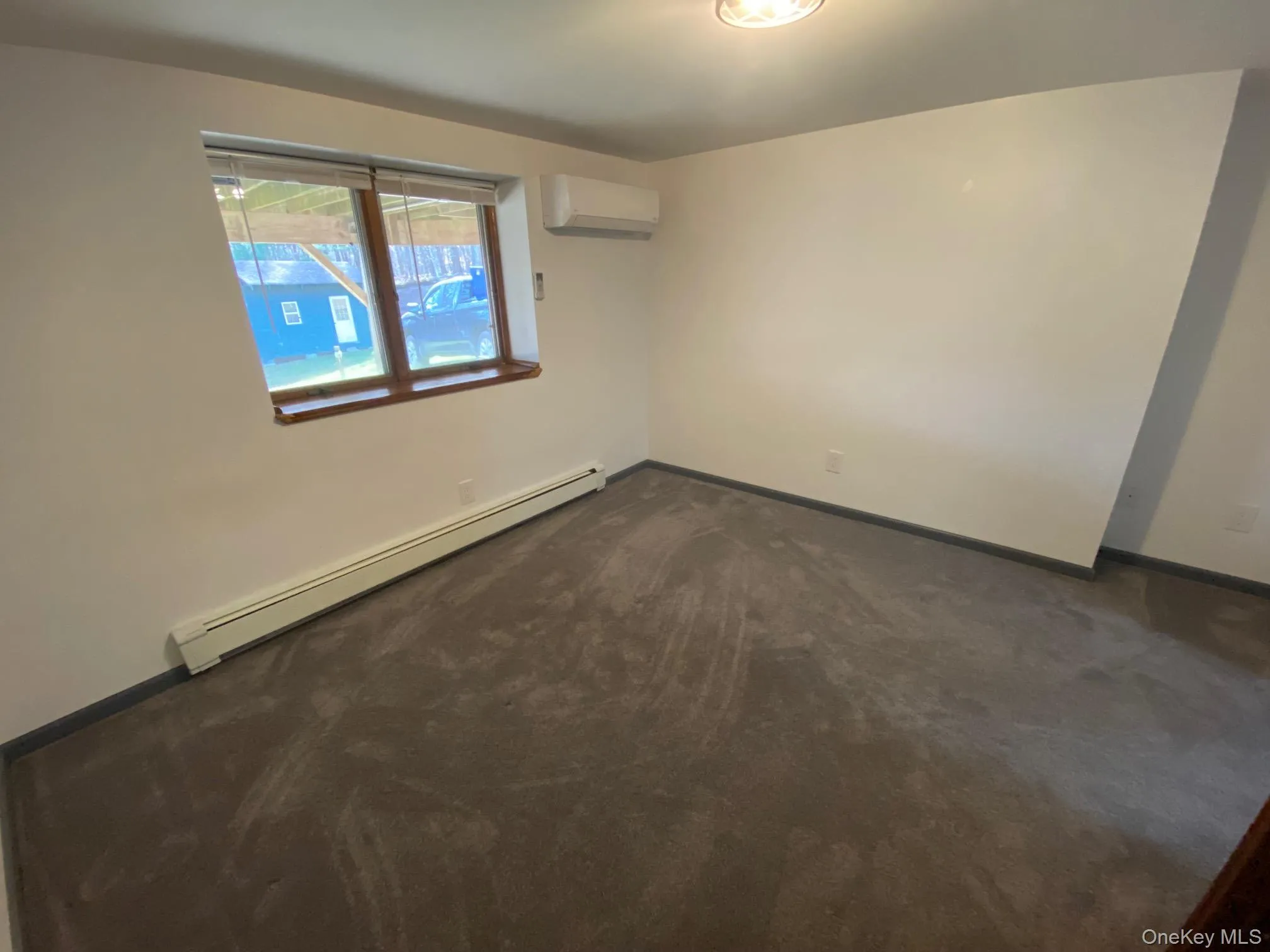 Bedroom featuring a wall mounted air conditioner, dark colored carpet, and a baseboard radiator Bedroom featuring a wall mounted air conditioner, dark colored carpet, and a baseboard radiator