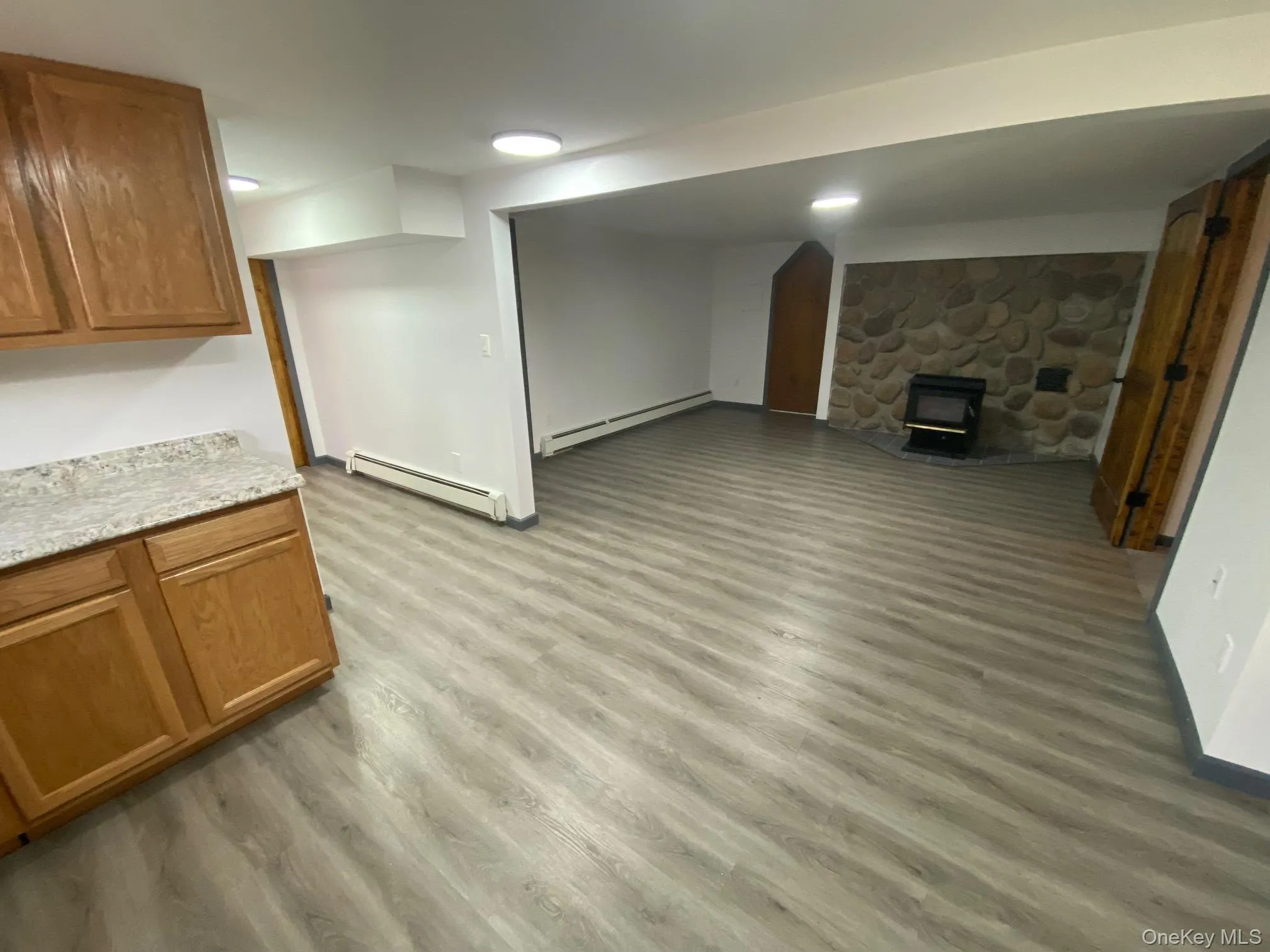 Unfurnished living room featuring a wood stove, light hardwood / wood-style floors, and a baseboard heating unit Unfurnished living room featuring a wood stove, light hardwood / wood-style floors, and a baseboard heating unit