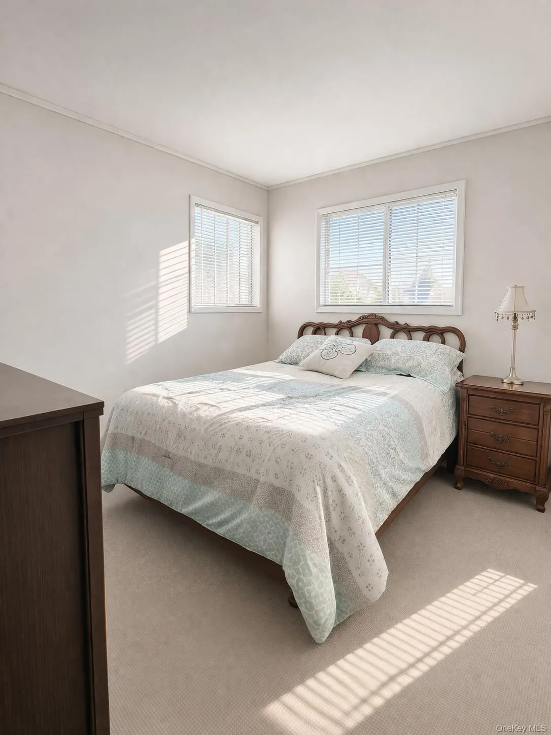 Carpeted bedroom featuring two windows with horizontal blinds, providing natural light Carpeted bedroom featuring two windows with horizontal blinds, providing natural light