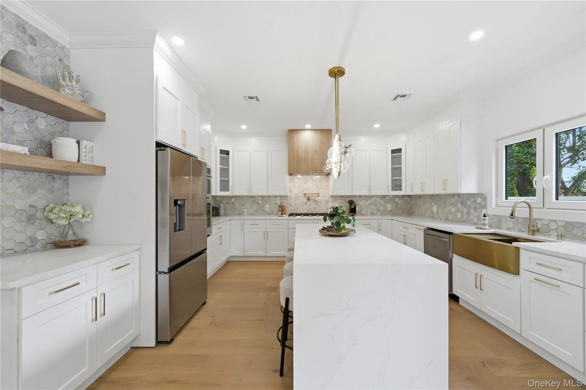Gourmet kitchen featuring a waterfall island, stainless steel appliances, a brass farmhouse sink, wood-finish flooring, and a hexagonal tile backsplash Gourmet kitchen featuring a waterfall island, stainless steel appliances, a brass farmhouse sink, wood-finish flooring, and a hexagonal tile backsplash