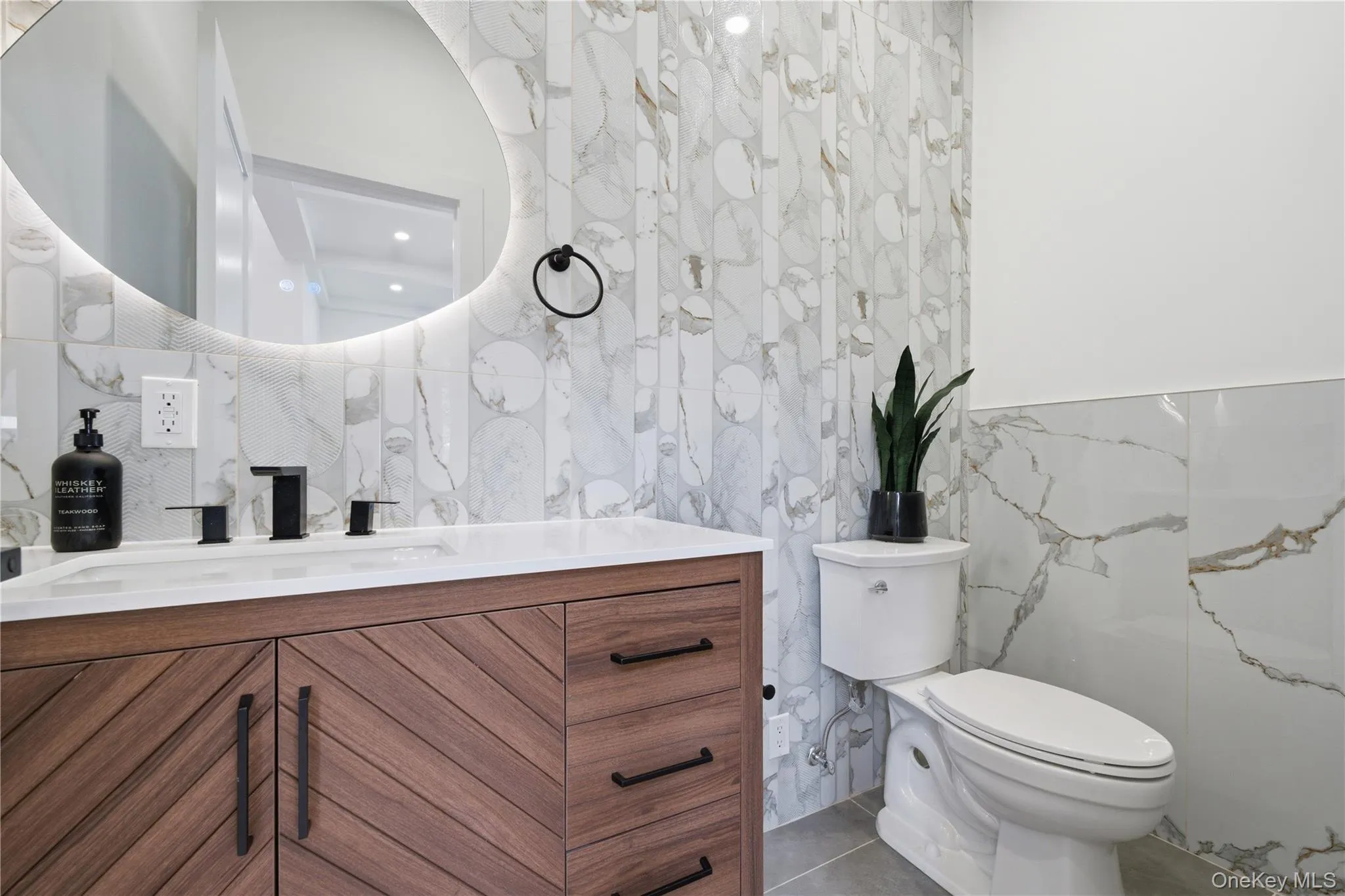 Contemporary bathroom featuring a wood-finish vanity with chevron detailing, a white integrated sink, and matte black fixtures Contemporary bathroom featuring a wood-finish vanity with chevron detailing, a white integrated sink, and matte black fixtures