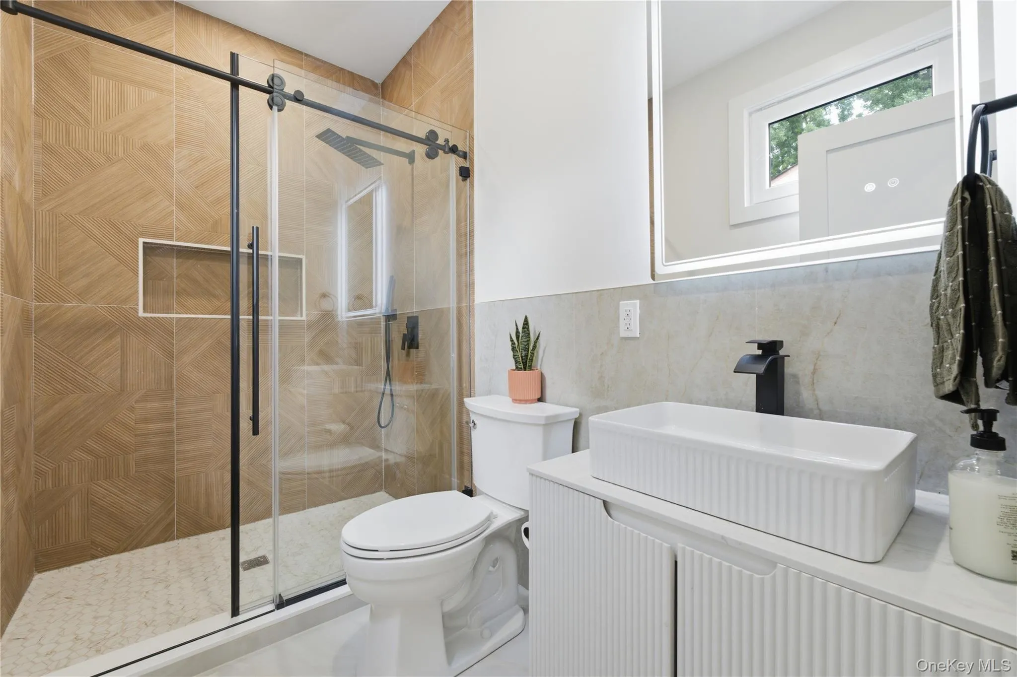 Modern bathroom featuring a glass-enclosed shower with geometric-patterned wall tiles, a rainfall showerhead, and a built-in shower niche Modern bathroom featuring a glass-enclosed shower with geometric-patterned wall tiles, a rainfall showerhead, and a built-in shower niche