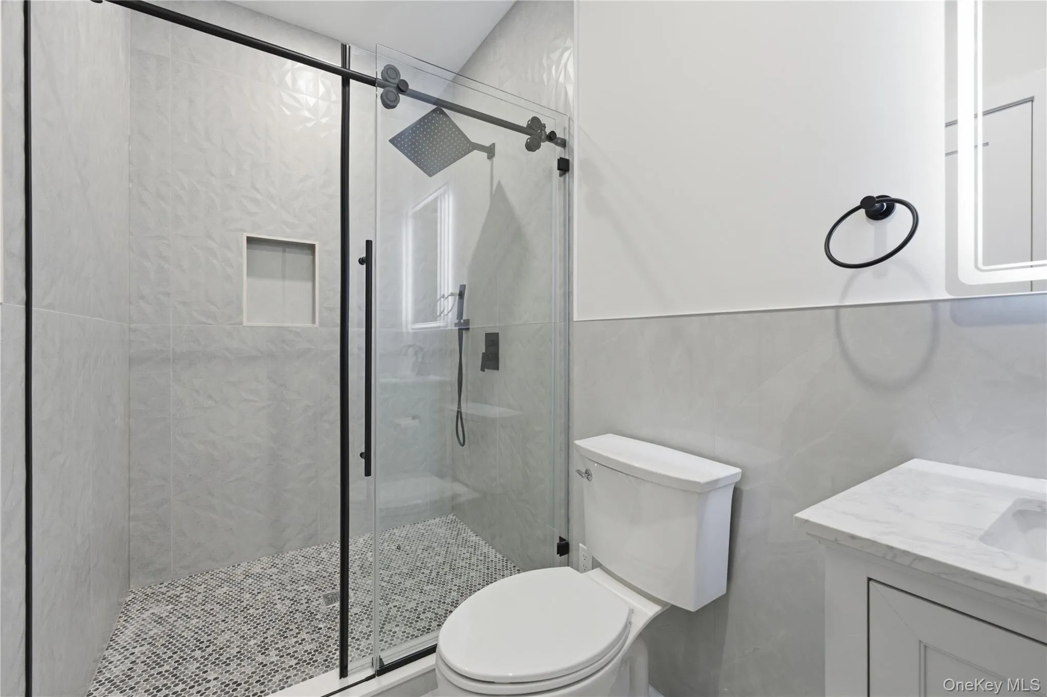Modern bathroom featuring a glass-enclosed shower with matte black fixtures, textured tile surround, and a pebble-mosaic floor Modern bathroom featuring a glass-enclosed shower with matte black fixtures, textured tile surround, and a pebble-mosaic floor