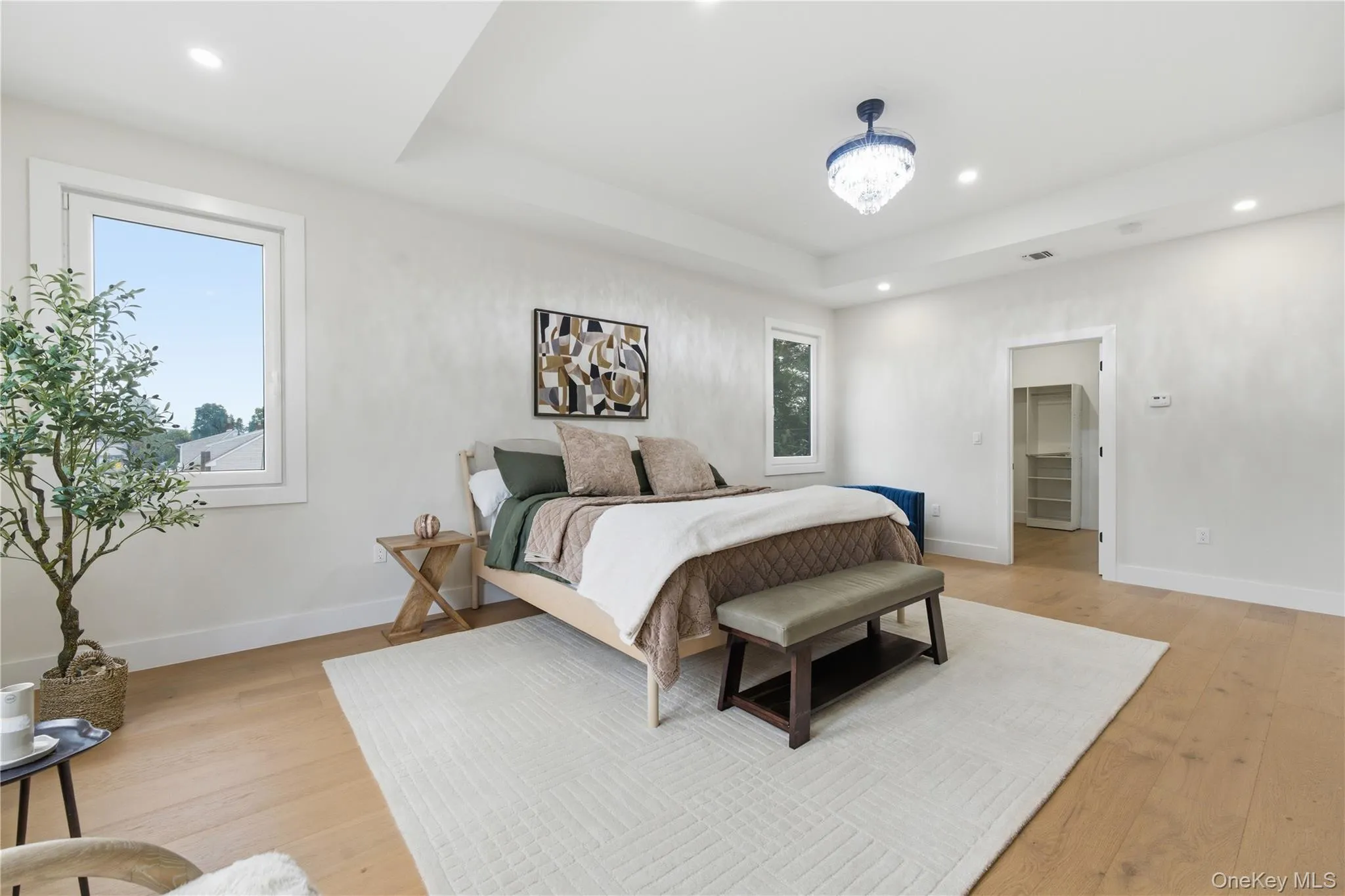Spacious room featuring light wood-finish flooring, a tray ceiling with recessed lighting, and a decorative chandelier Spacious room featuring light wood-finish flooring, a tray ceiling with recessed lighting, and a decorative chandelier