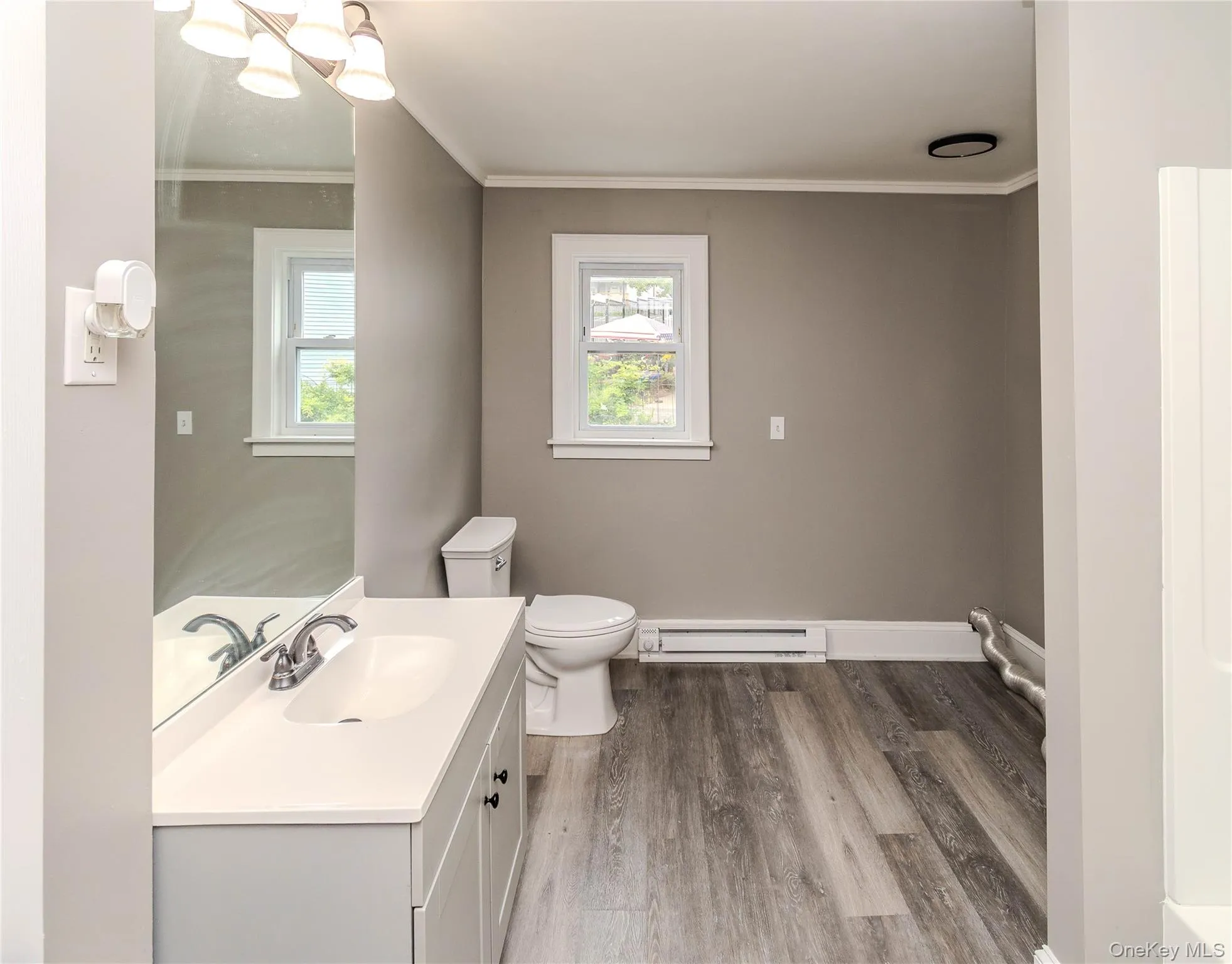 Light gray vanity with an integrated sink, chrome faucet, wall-mounted mirror, and wood-finish flooring Light gray vanity with an integrated sink, chrome faucet, wall-mounted mirror, and wood-finish flooring