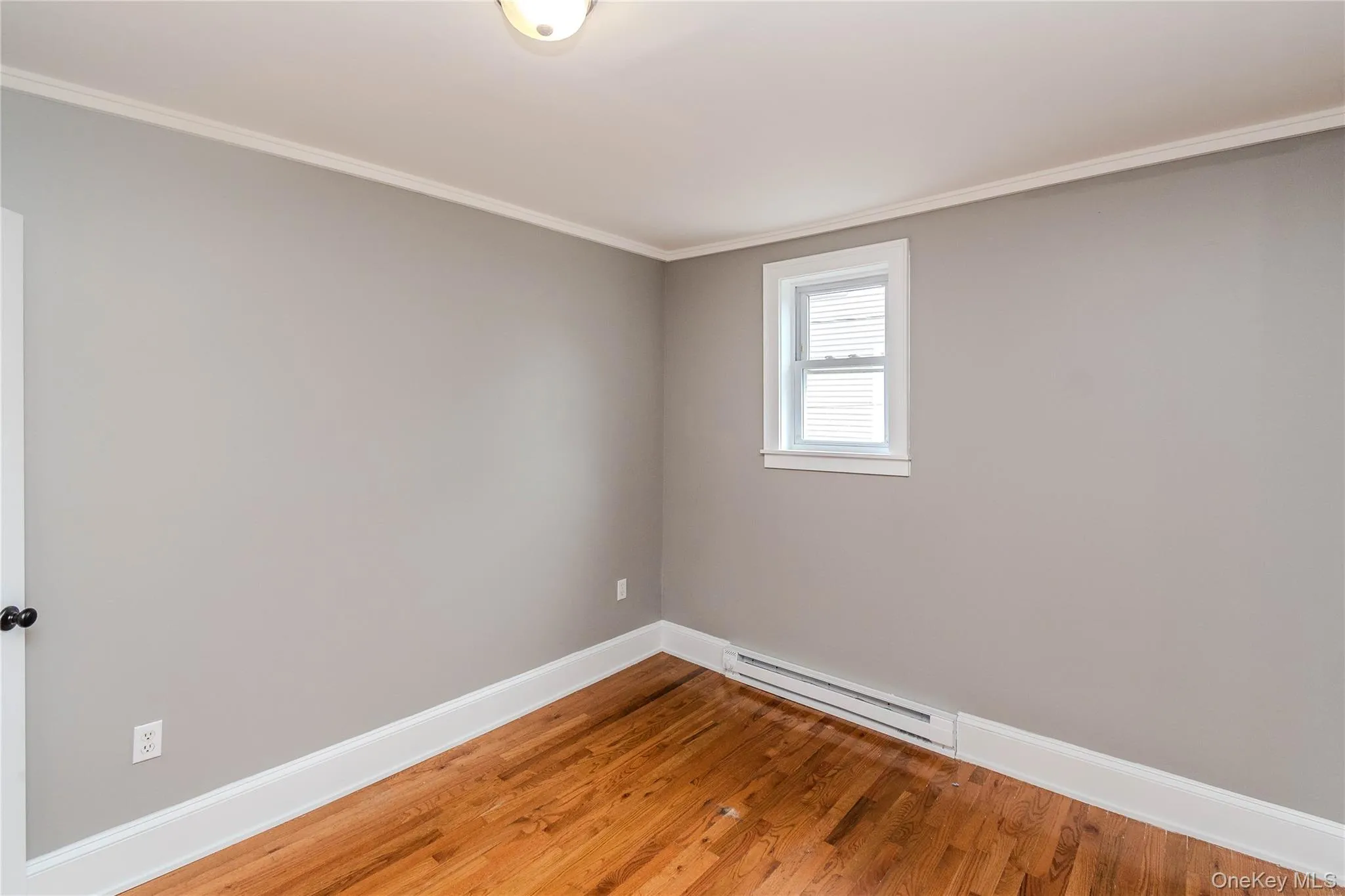 Hardwood flooring, neutral wall color, white trim, single window, and flush mount ceiling light Hardwood flooring, neutral wall color, white trim, single window, and flush mount ceiling light