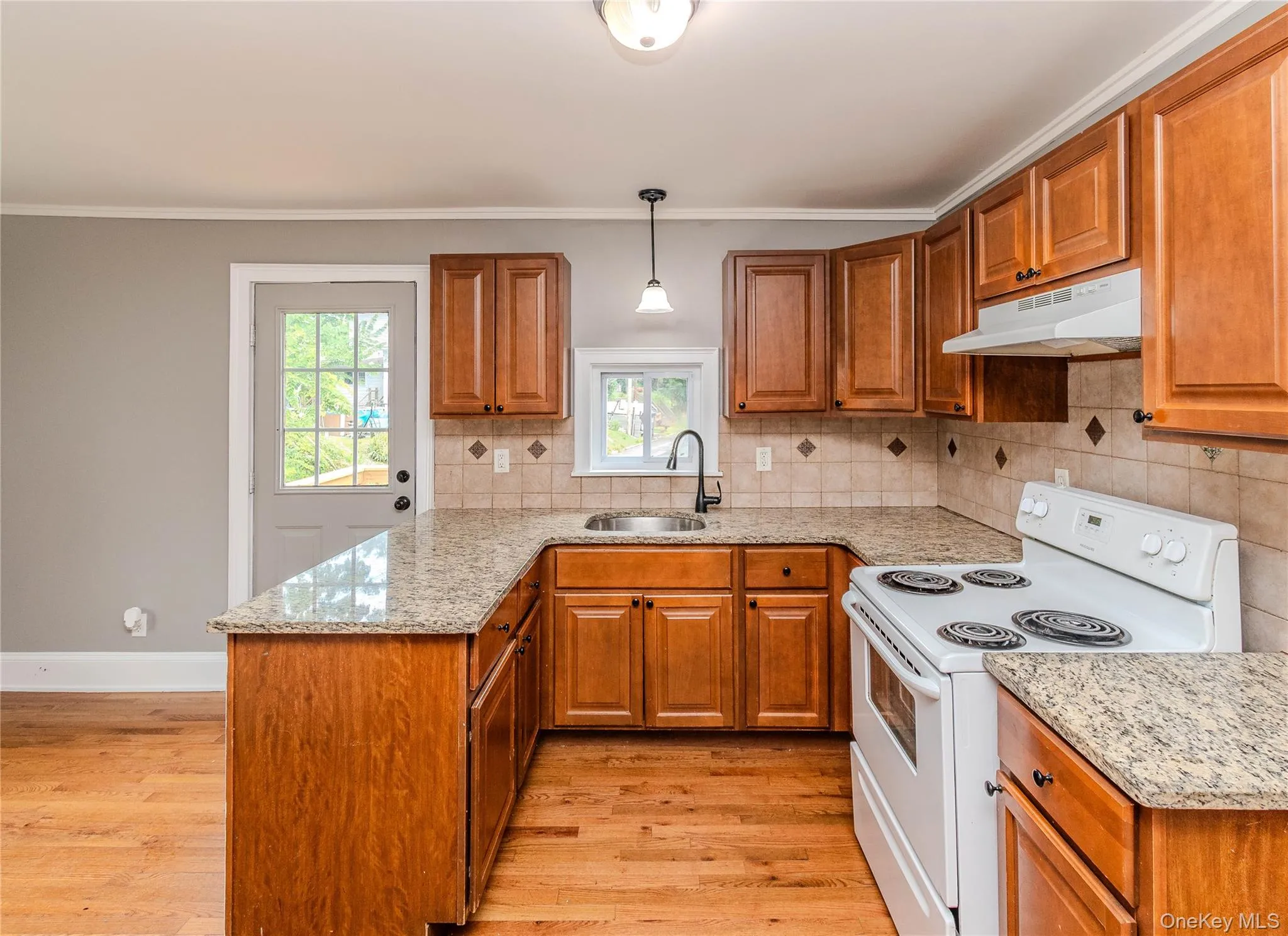U-shaped kitchen featuring wood-finish cabinetry, granite-style countertops, a tile backsplash, and wood-finish flooring U-shaped kitchen featuring wood-finish cabinetry, granite-style countertops, a tile backsplash, and wood-finish flooring
