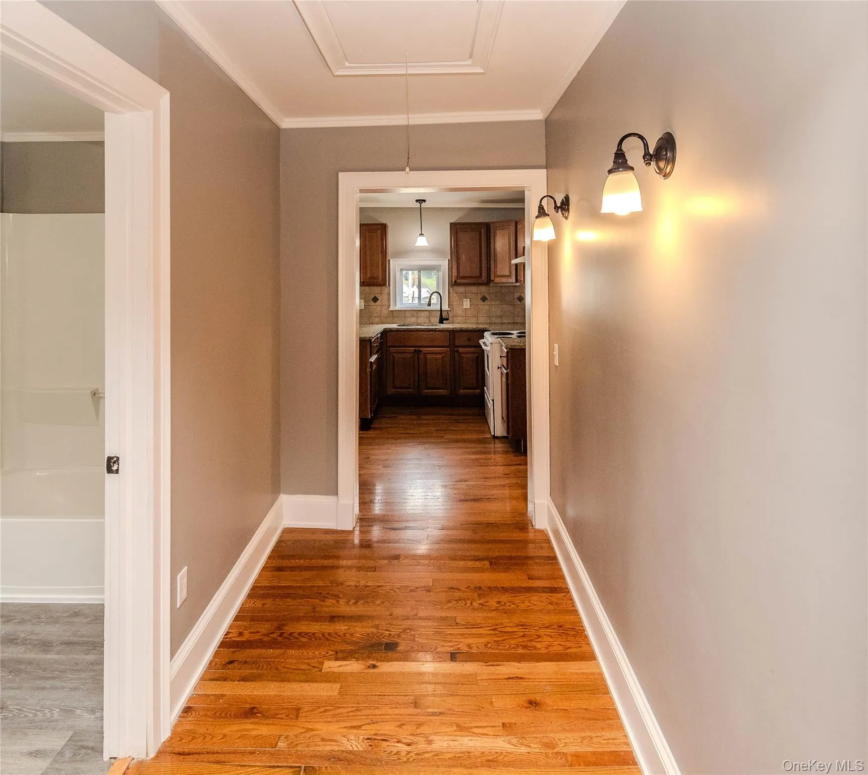 Hardwood flooring, crown molding, wall-mounted sconces, and white trim Hardwood flooring, crown molding, wall-mounted sconces, and white trim