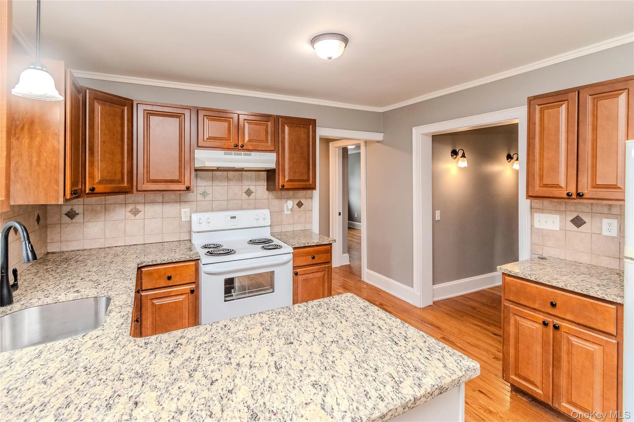 Kitchen featuring wood cabinetry, granite countertops, tile backsplash, stainless steel sink, and hardwood flooring Kitchen featuring wood cabinetry, granite countertops, tile backsplash, stainless steel sink, and hardwood flooring