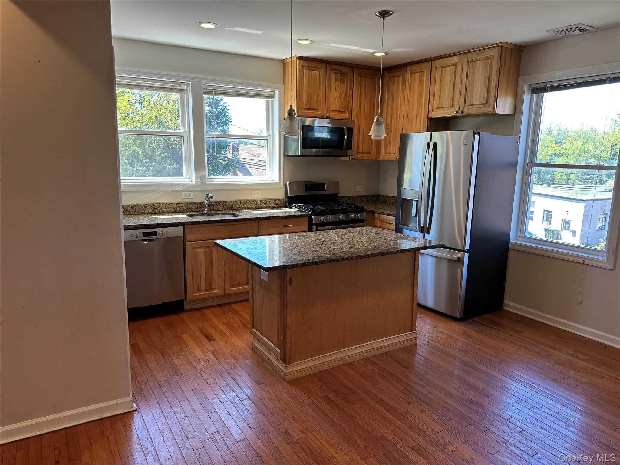 Kitchen featuring wood-finish flooring, a central island with a granite-style countertop, and stainless steel appliances Kitchen featuring wood-finish flooring, a central island with a granite-style countertop, and stainless steel appliances