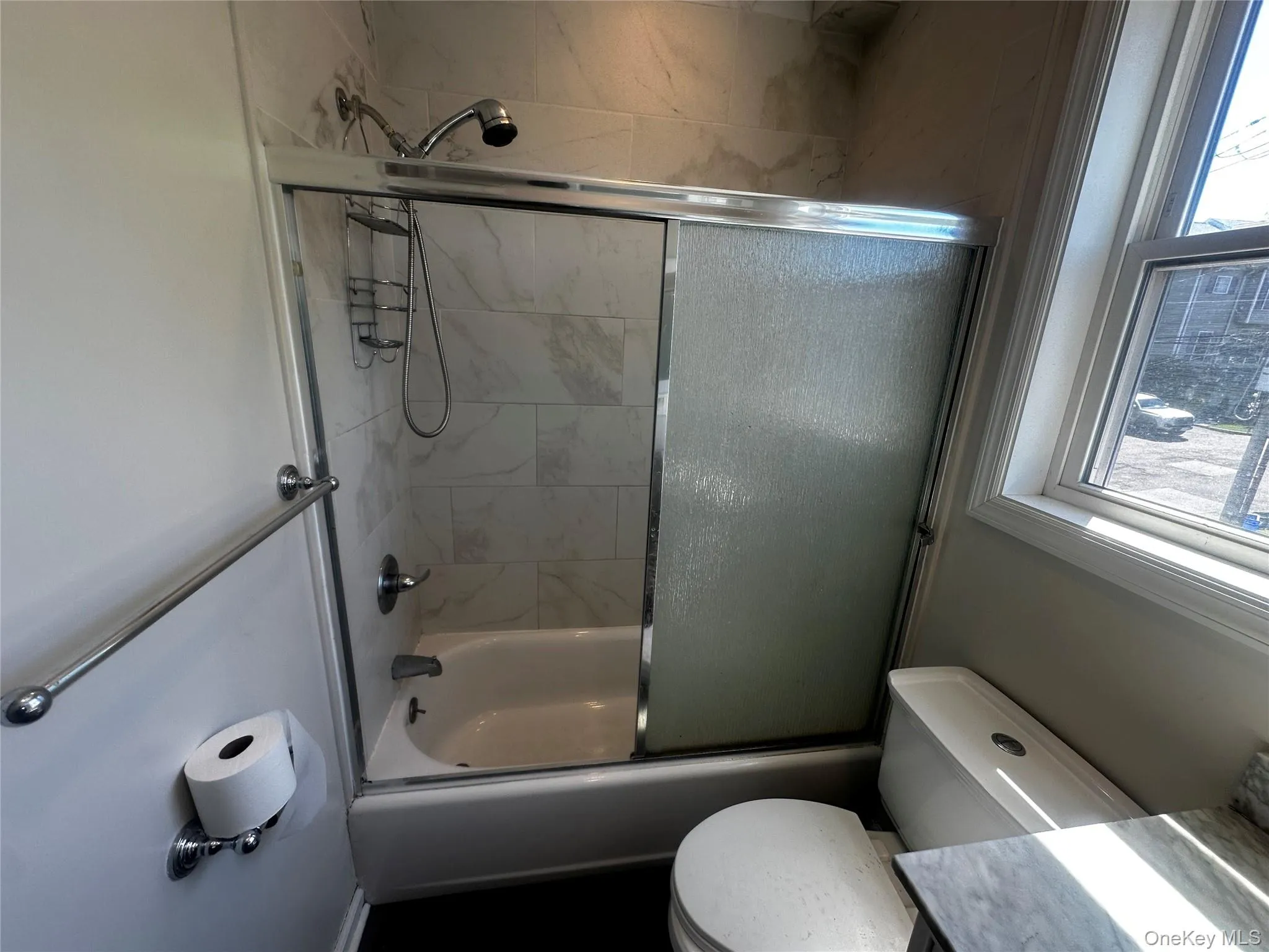 Full bathroom featuring a tub and shower combination with sliding glass doors, white subway tile surround, and a chrome shower head Full bathroom featuring a tub and shower combination with sliding glass doors, white subway tile surround, and a chrome shower head