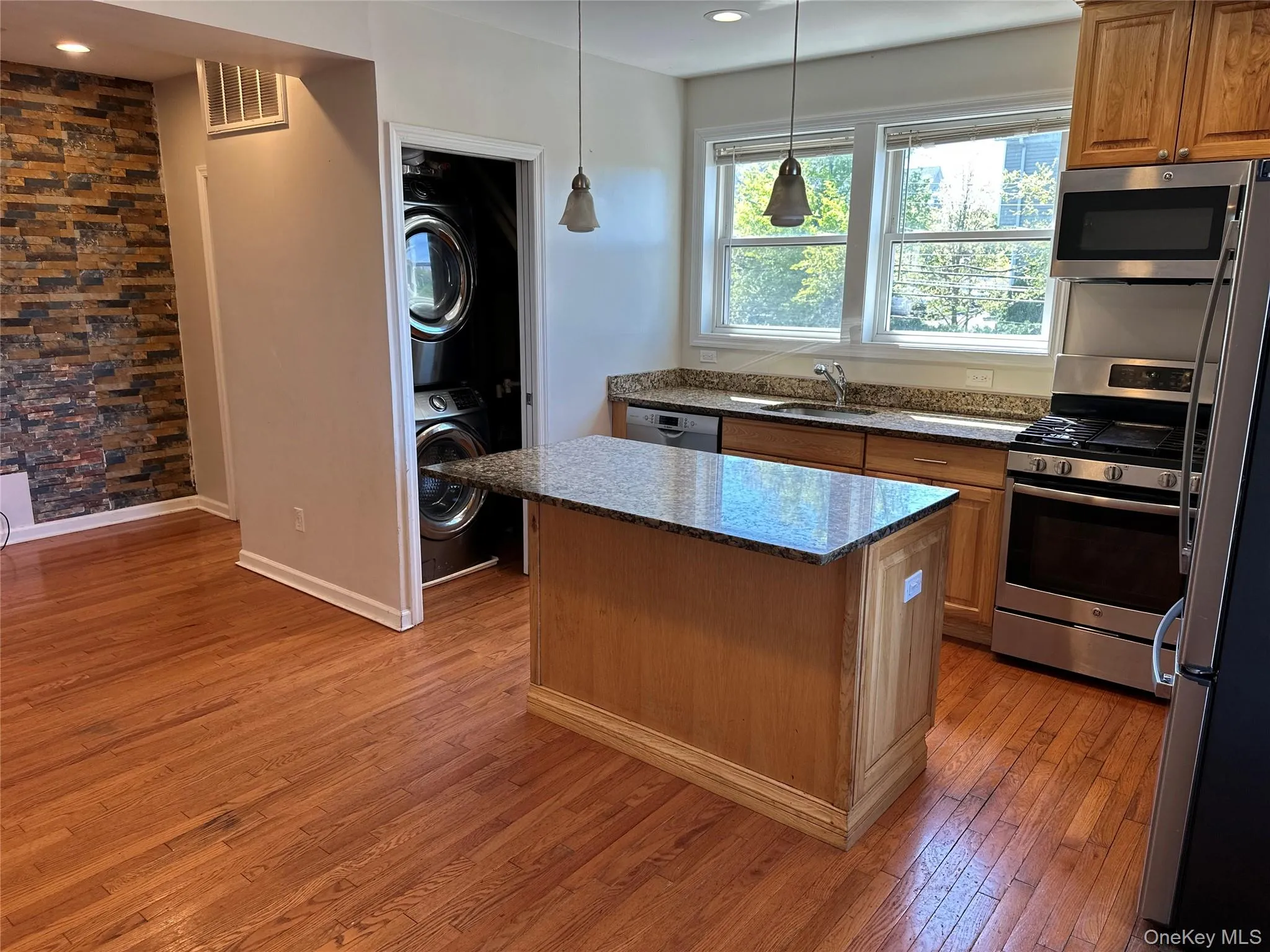 Kitchen featuring an island with a granite countertop, light wood cabinetry, stainless steel appliances, and wood-finish flooring and Washer/Dryer Kitchen featuring an island with a granite countertop, light wood cabinetry, stainless steel appliances, and wood-finish flooring and Washer/Dryer
