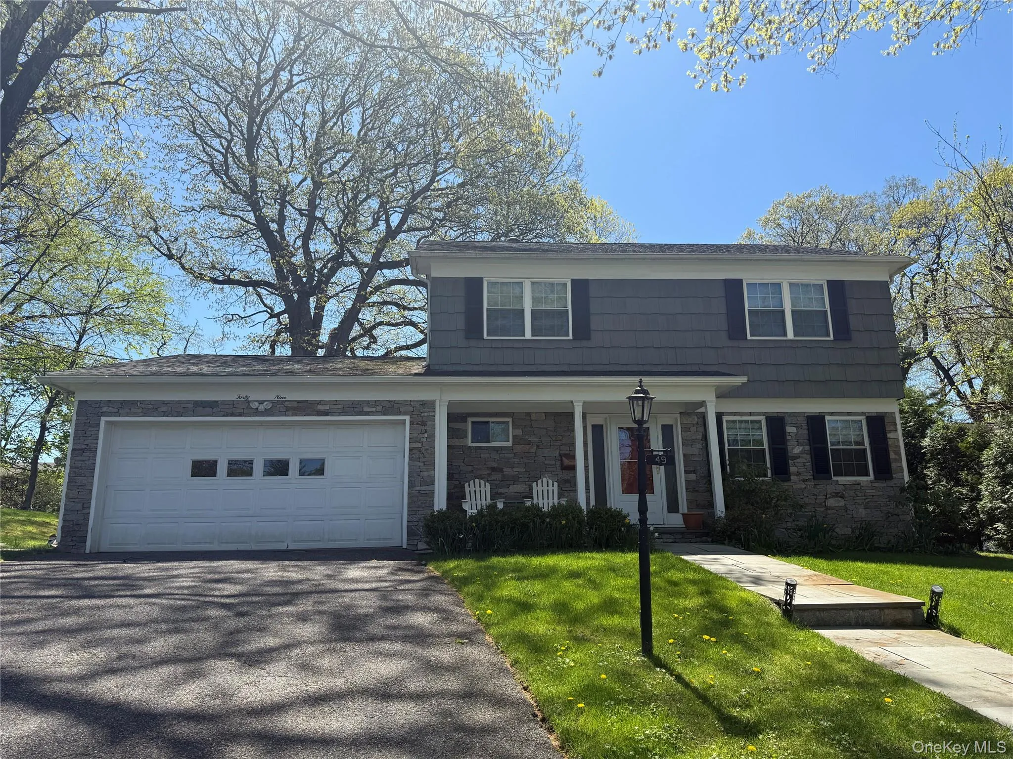 View of front of property featuring a front yard, driveway, stone siding, and an attached garage View of front of property featuring a front yard, driveway, stone siding, and an attached garage