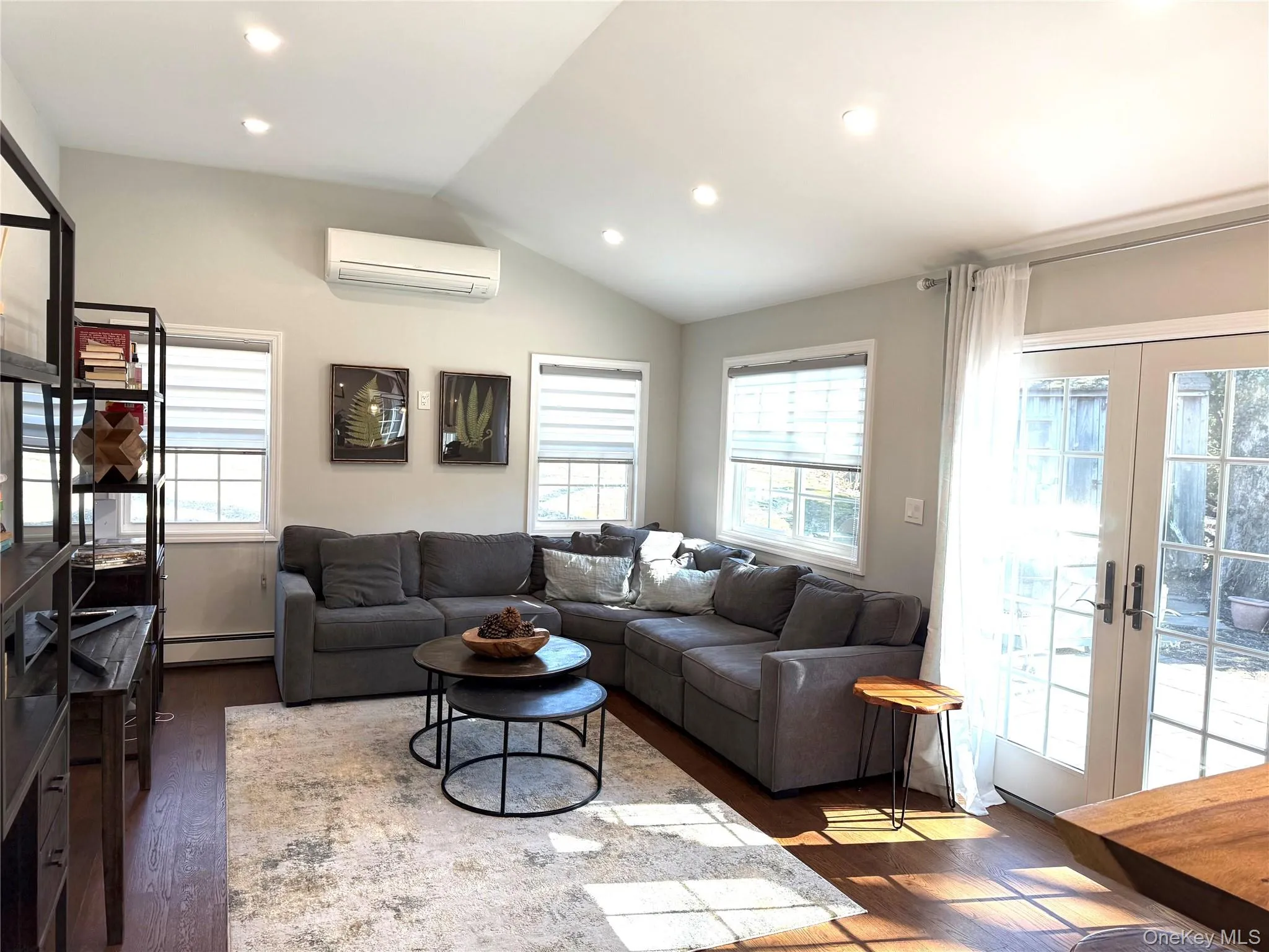 Large family room featuring vaulted ceiling, plenty of natural light, french doors, baseboard heating, and a wall mounted air conditioner Large family room featuring vaulted ceiling, plenty of natural light, french doors, baseboard heating, and a wall mounted air conditioner