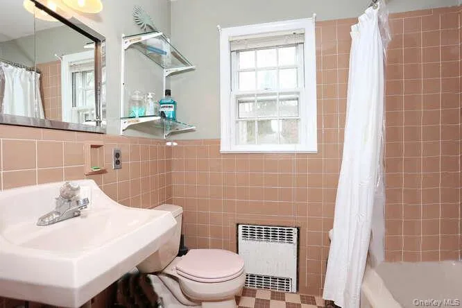 Bathroom featuring a sink, tile walls, toilet, shower / bath combo with shower curtain, and radiator Bathroom featuring a sink, tile walls, toilet, shower / bath combo with shower curtain, and radiator