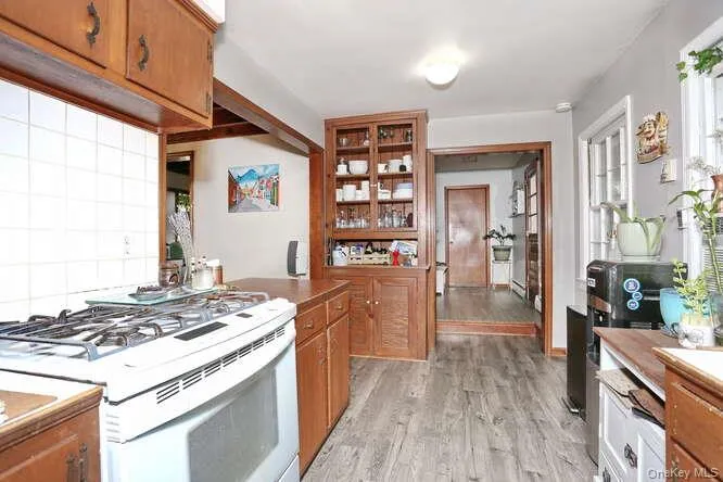 Kitchen with glass insert cabinets, white gas stove, brown cabinets, light wood finished floors, and decorative backsplash Kitchen with glass insert cabinets, white gas stove, brown cabinets, light wood finished floors, and decorative backsplash