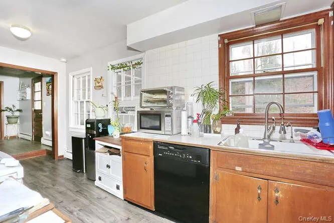 Kitchen featuring black dishwasher, stainless steel microwave, light countertops, a sink, and light wood finished floors Kitchen featuring black dishwasher, stainless steel microwave, light countertops, a sink, and light wood finished floors