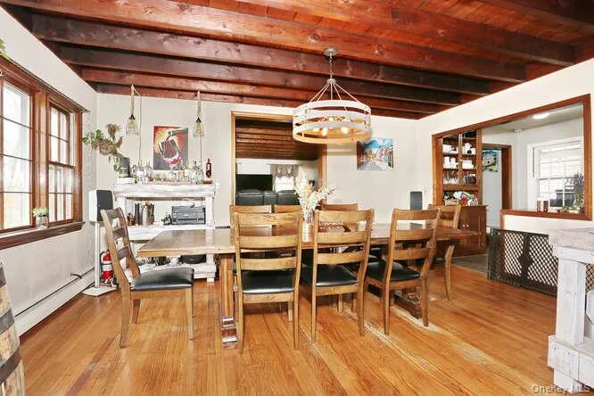 Dining room featuring beamed ceiling, an inviting chandelier, wood finished floors, and a baseboard heating unit Dining room featuring beamed ceiling, an inviting chandelier, wood finished floors, and a baseboard heating unit