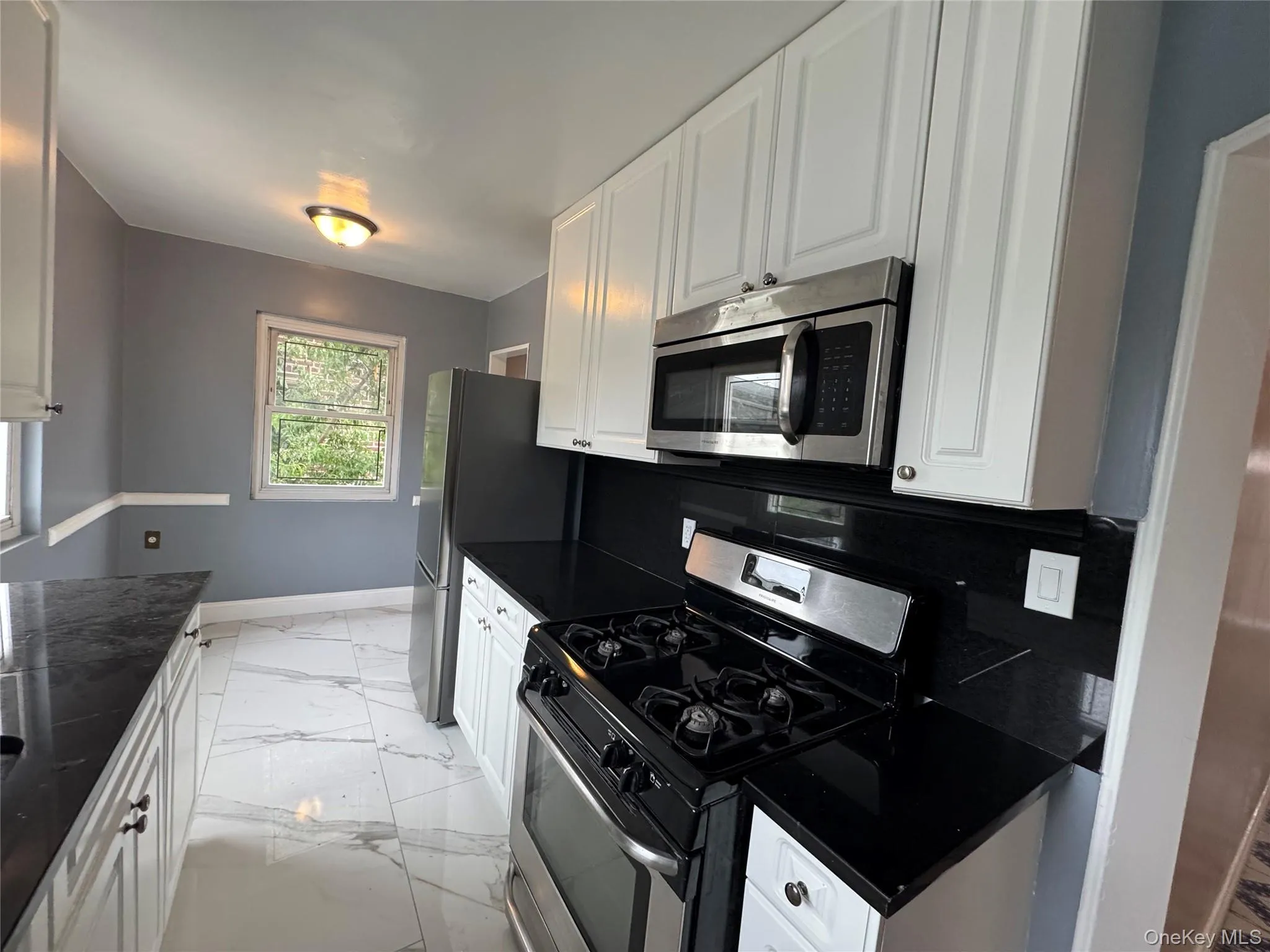 Kitchen featuring stainless steel appliances, light marble finish flooring, and white cabinetry Kitchen featuring stainless steel appliances, light marble finish flooring, and white cabinetry