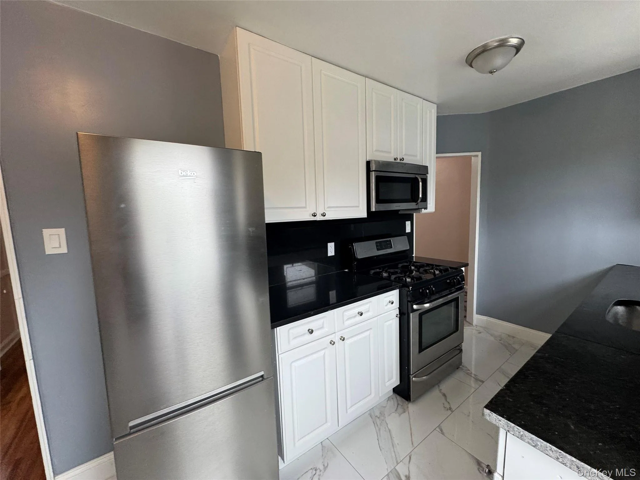Kitchen with light marble finish flooring, stainless steel appliances, white cabinetry, and dark countertops Kitchen with light marble finish flooring, stainless steel appliances, white cabinetry, and dark countertops