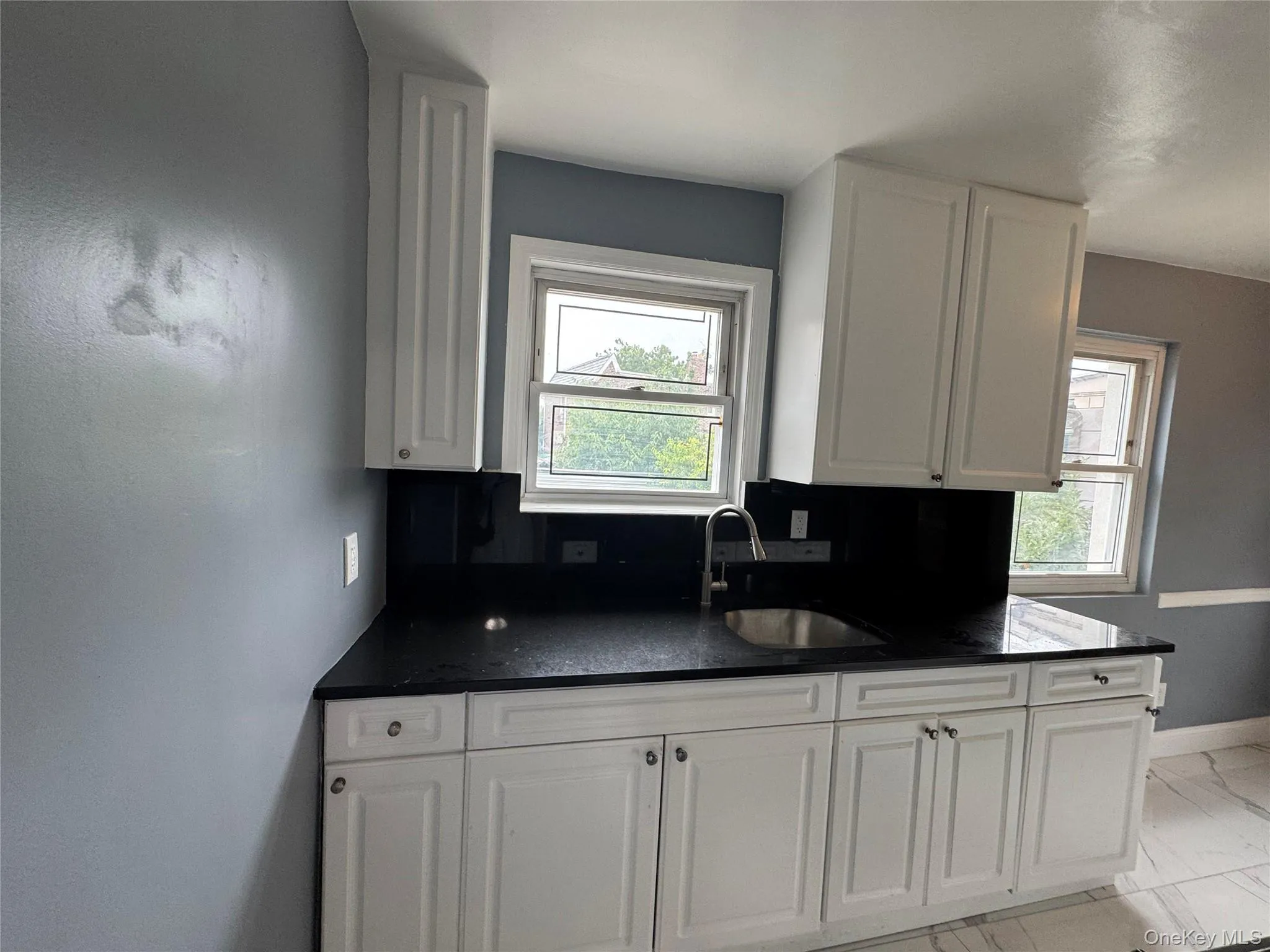 Kitchen featuring dark countertops, white cabinets, and light marble finish flooring Kitchen featuring dark countertops, white cabinets, and light marble finish flooring