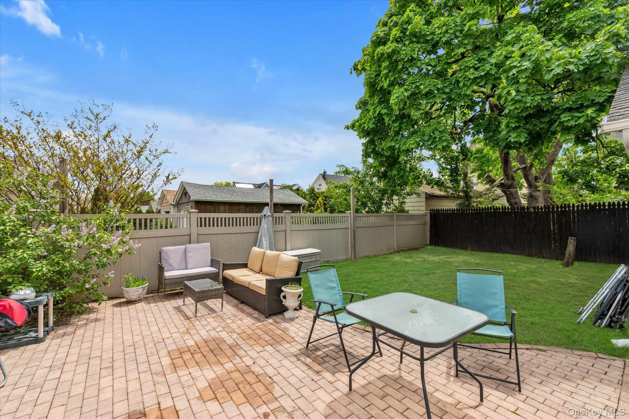 Expansive outdoor space featuring a red brick paver patio, lawn, and a light-toned privacy fence Expansive outdoor space featuring a red brick paver patio, lawn, and a light-toned privacy fence
